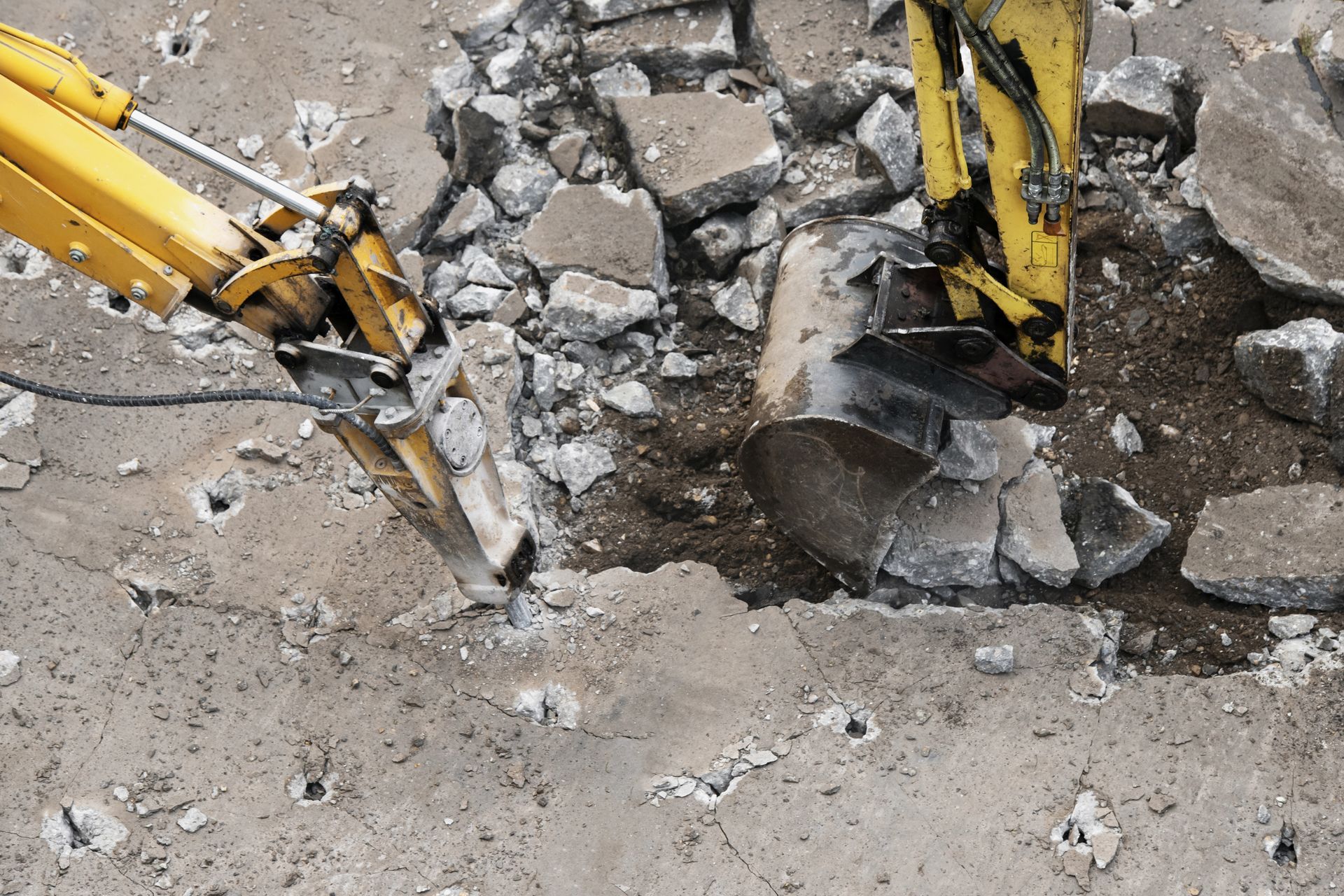 Escavatore giallo che demolisce una superficie di cemento, rompendola in pezzi.