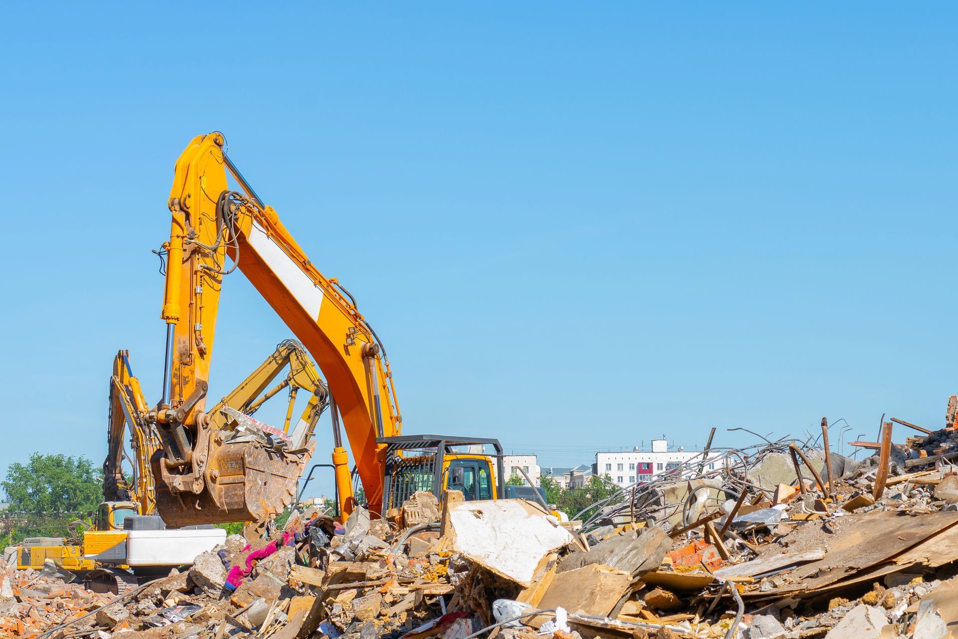 Un escavatore giallo rimuove i detriti da un cantiere di demolizione sotto un cielo azzurro.