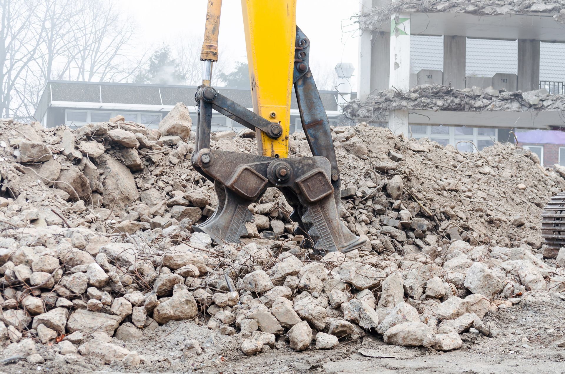 Braccio di un escavatore giallo che afferra un cumulo di macerie in un cantiere edile.