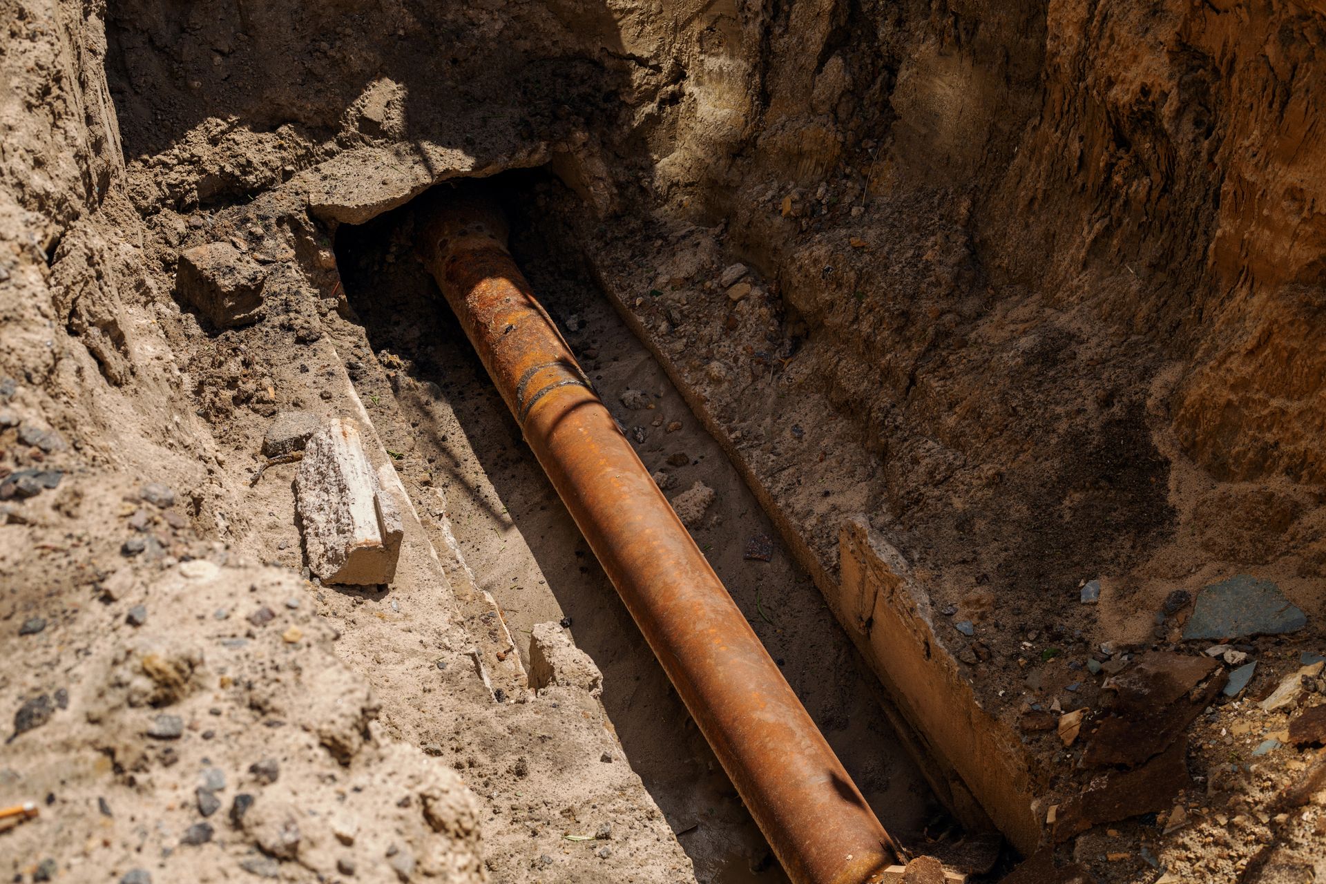 Tubi metallici arrugginiti in una trincea, probabilmente per lavori di manutenzione sotterranea.