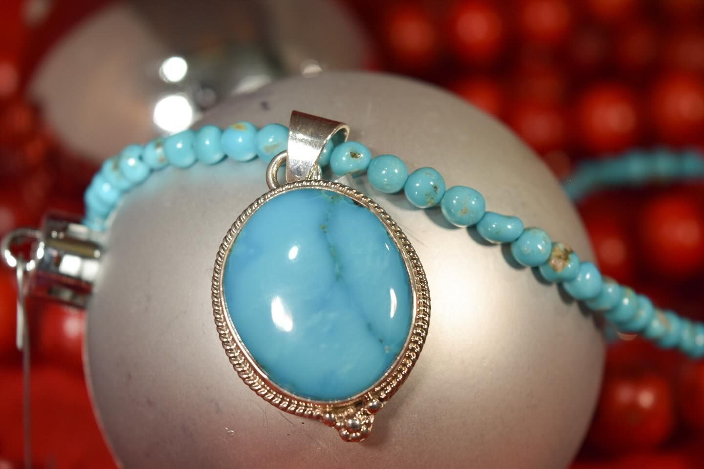 Turquoise pendant on a silver ornament with turquoise bead necklace, red background.