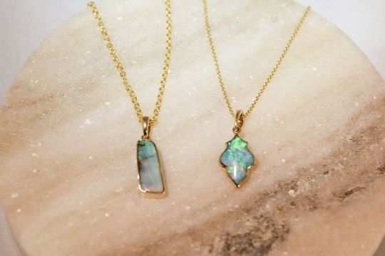 Two gold necklaces with opal pendants on a marble surface.