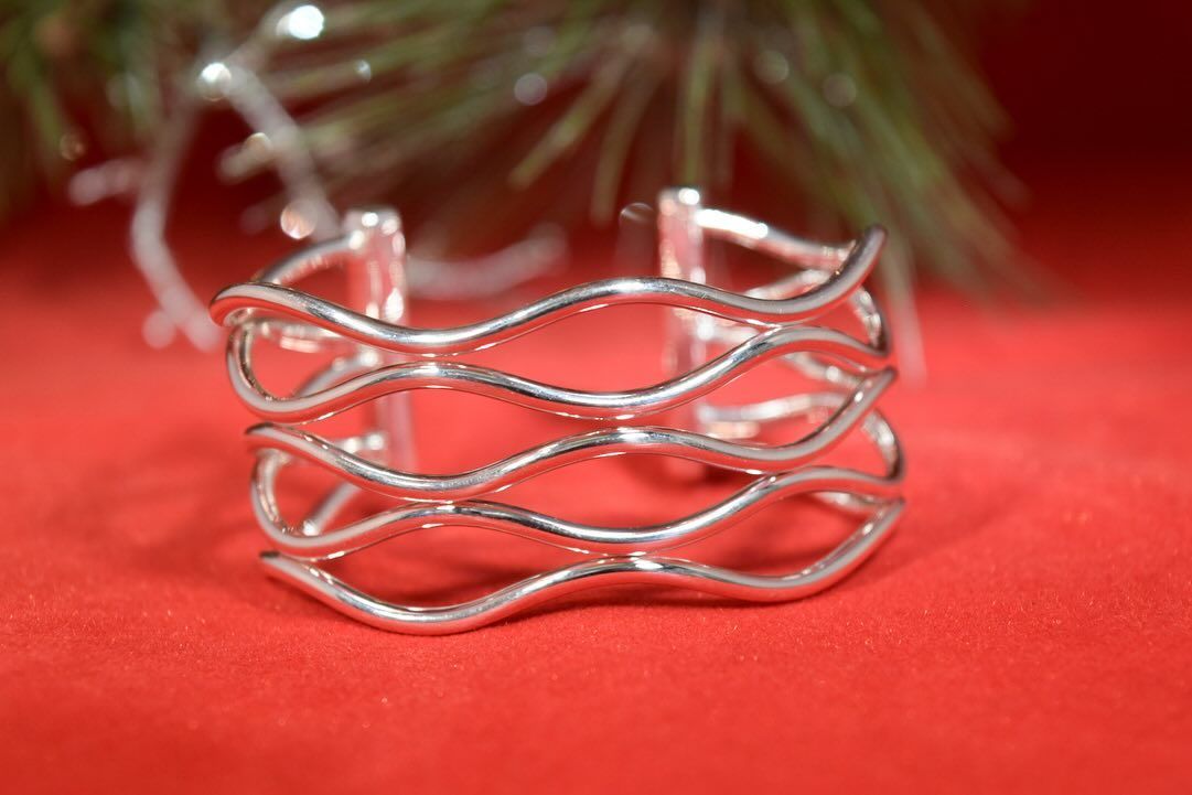 Silver wavy cuff bracelet on a red surface, with a blurred festive backdrop.
