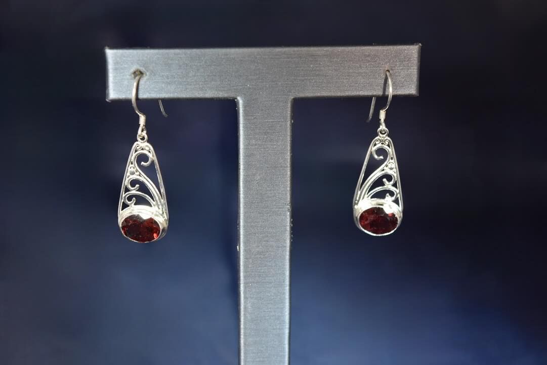 Silver filigree teardrop earrings with red-brown gemstone centers, displayed on a silver jewelry stand.