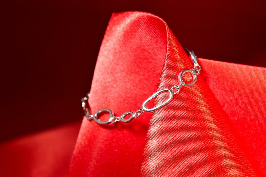 Silver bracelet resting on a red satin cloth.