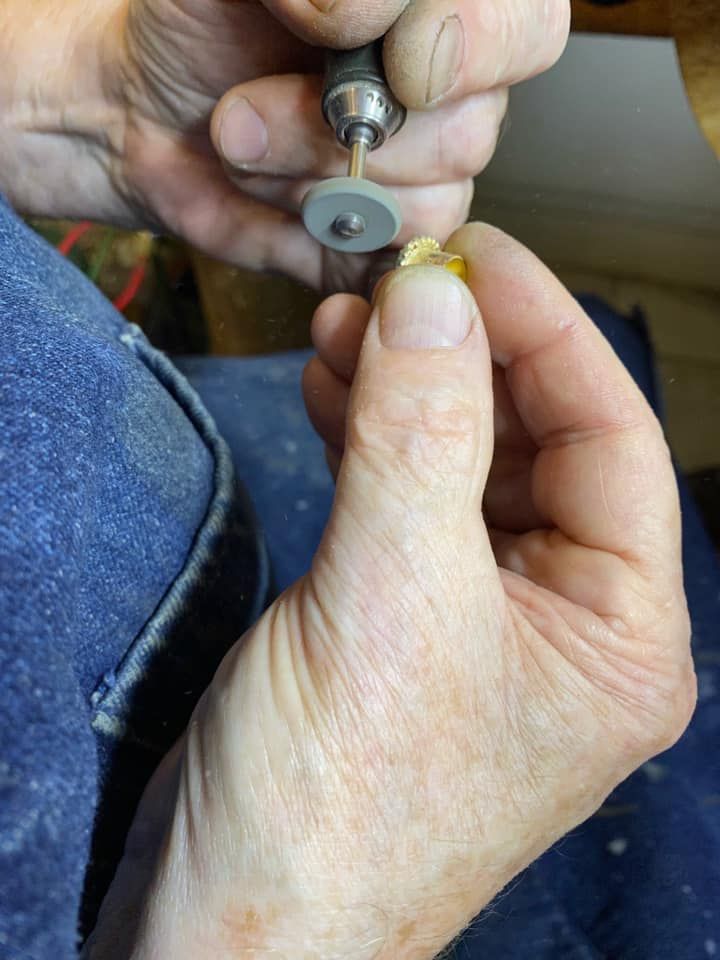 Person using a rotary tool to work on a small, yellow object held in their hand.