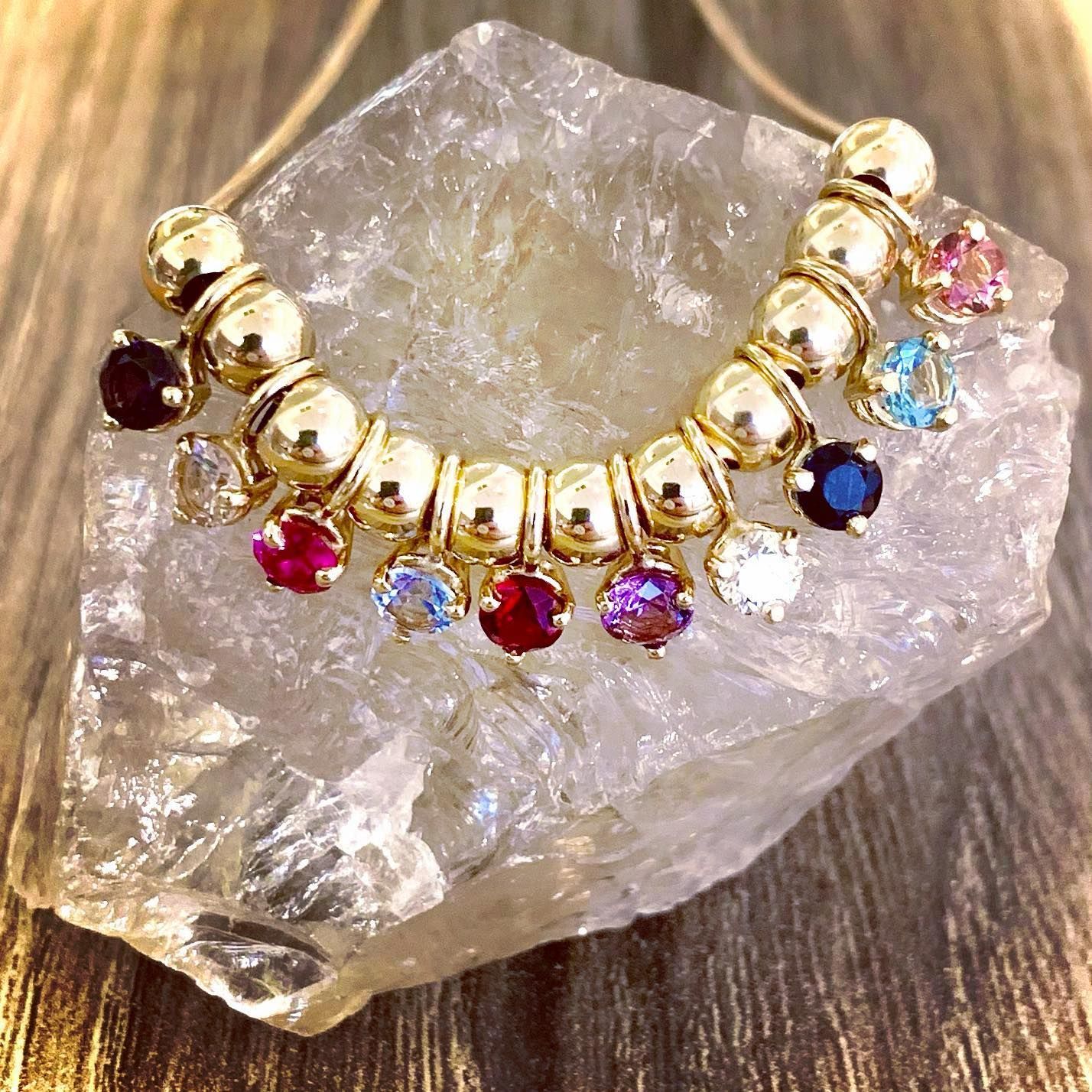 Gold beaded necklace with colorful gemstone charms, displayed on a quartz crystal.