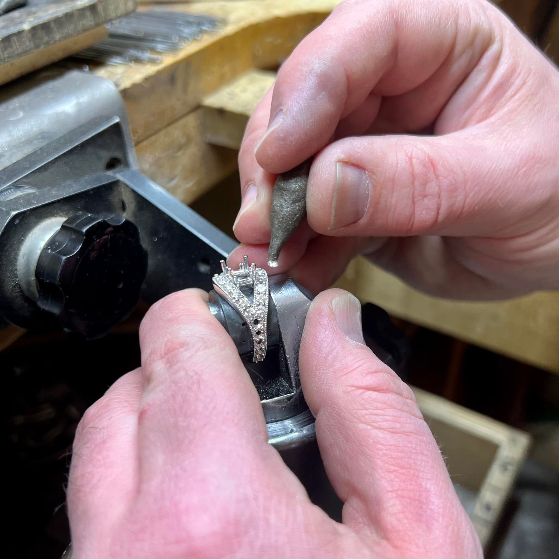 Hands of a jeweler working on a ring with a tool. The ring is held in place by a clamp.