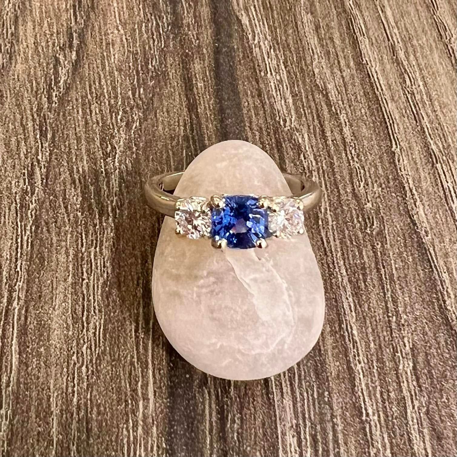 Ring with a blue sapphire center stone and two white side stones set on a light pink stone.