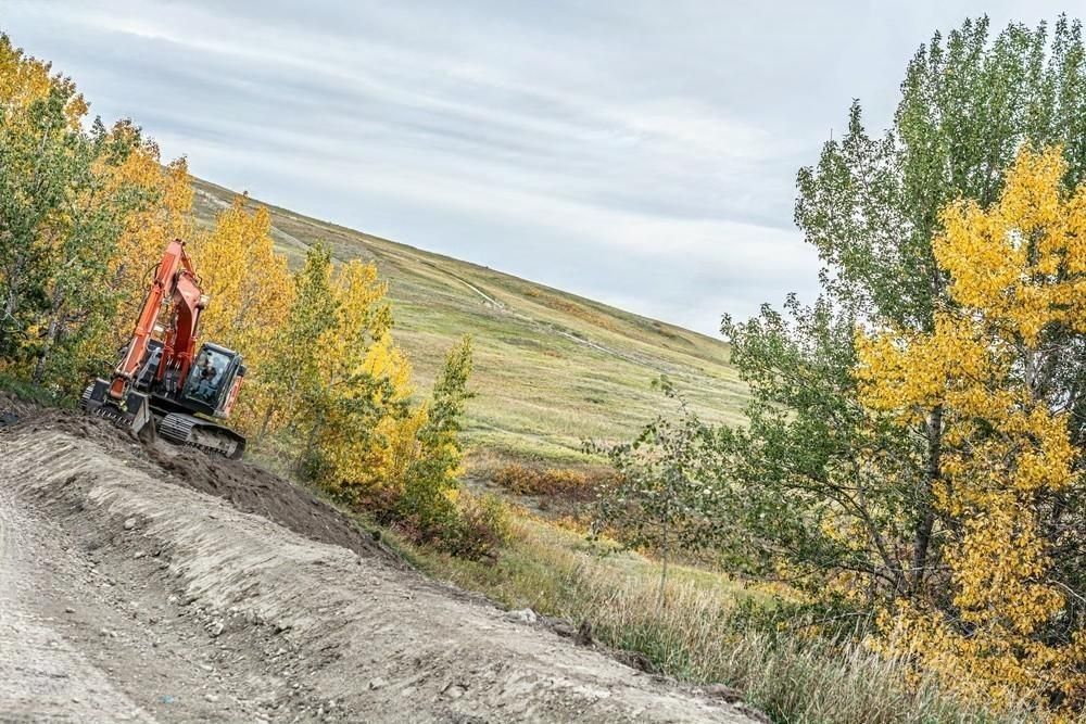 An excavator is driving down a dirt road in the woods.