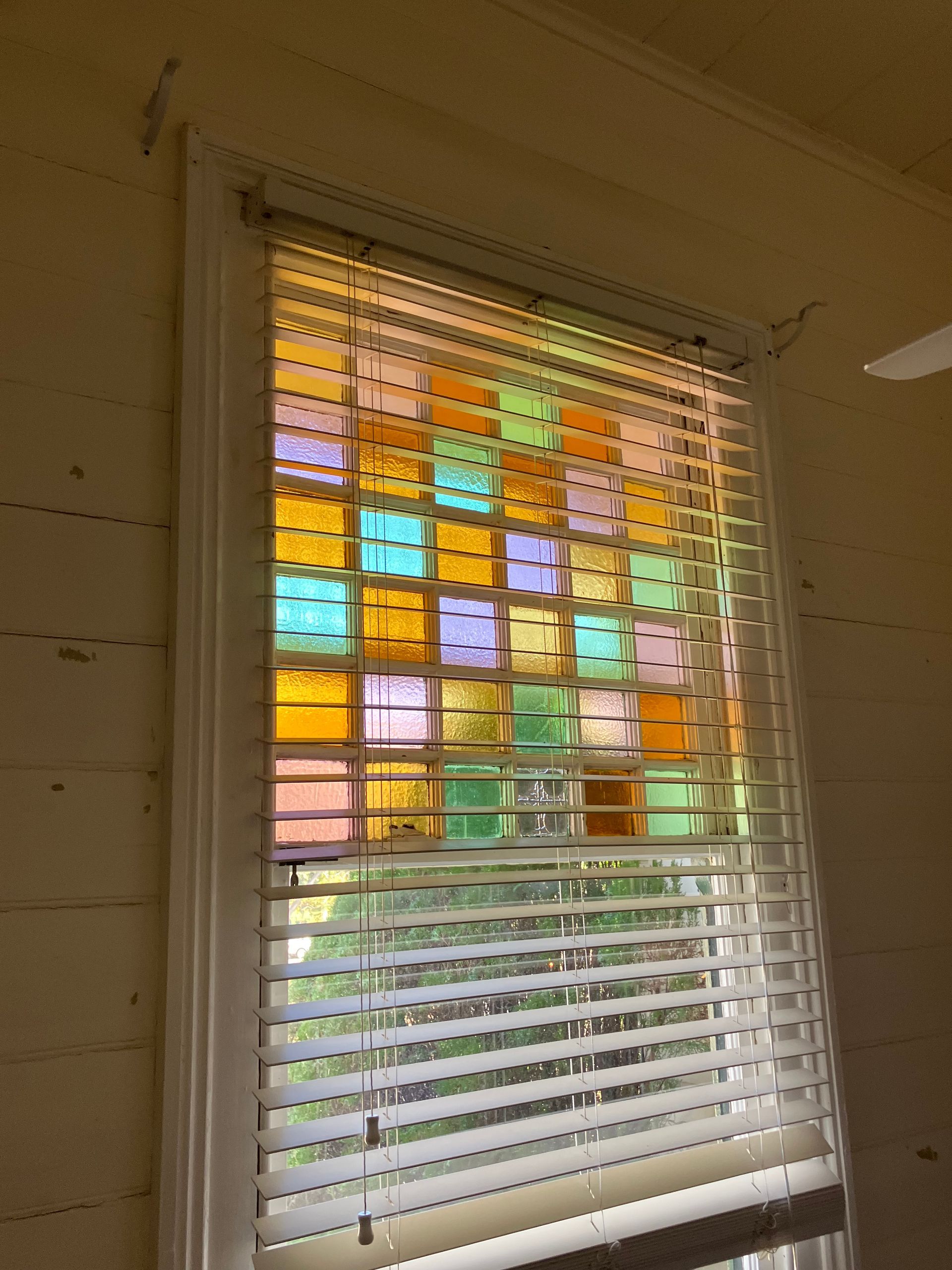 Window with white venetians blinds and colorful stained glass sqaures on the glass