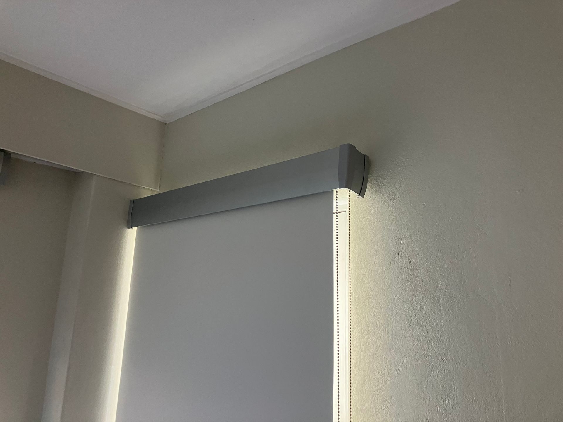 Closed white window blind with gray valance in a beige room corner