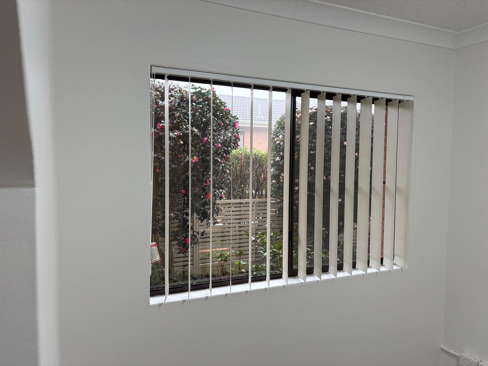 White room with a window and vertical blinds, showing greenery outside