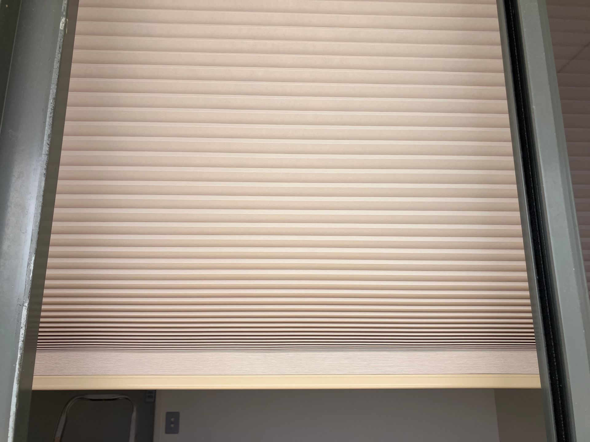 Closed beige window blinds framed by gray walls, with a small gap at the bottom.