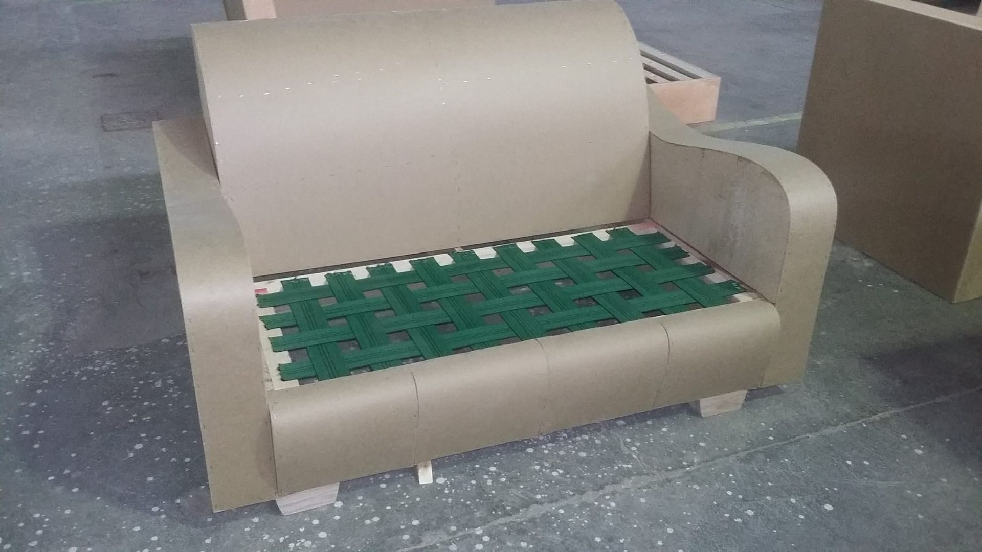 Un divano di cartone con un cuscino verde è appoggiato su un pavimento di cemento.