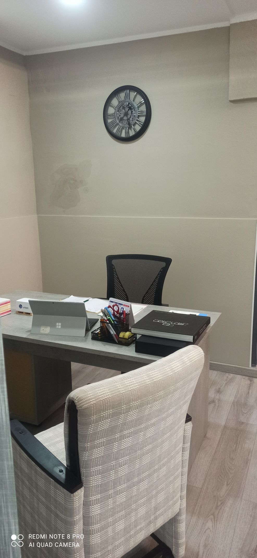 Una stanza con una scrivania, delle sedie e un orologio sul muro.