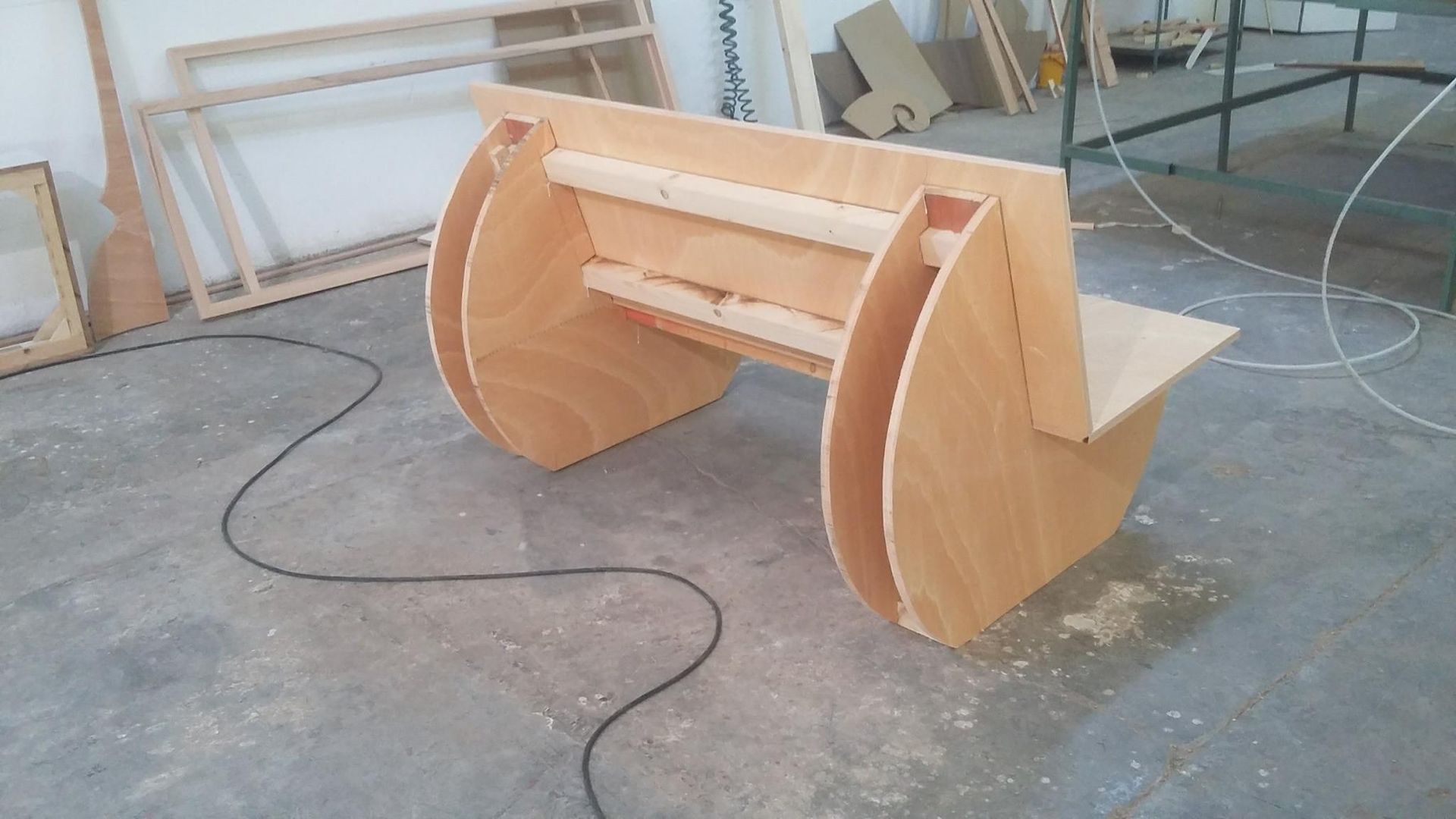 Una panca di legno è appoggiata su un pavimento di cemento in una stanza.