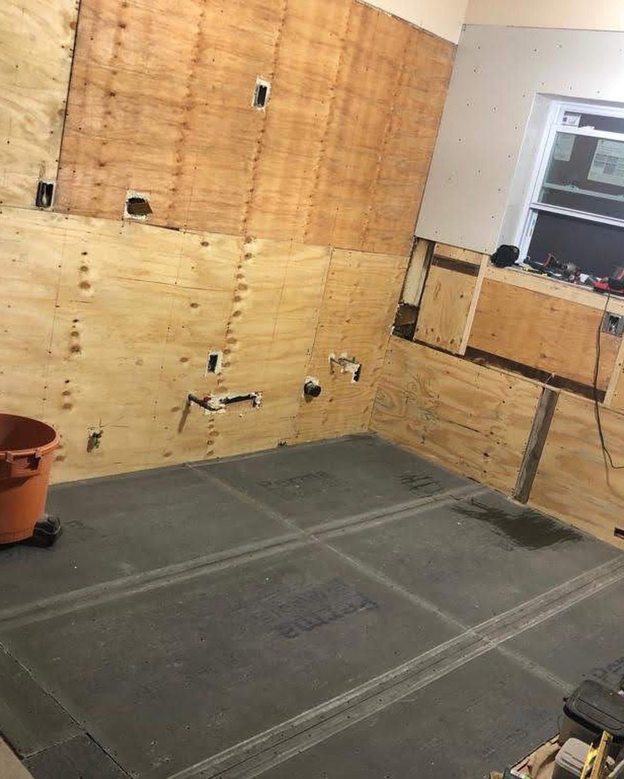 Construction site: plywood walls, dark flooring, orange bucket. Empty room with unfinished elements.