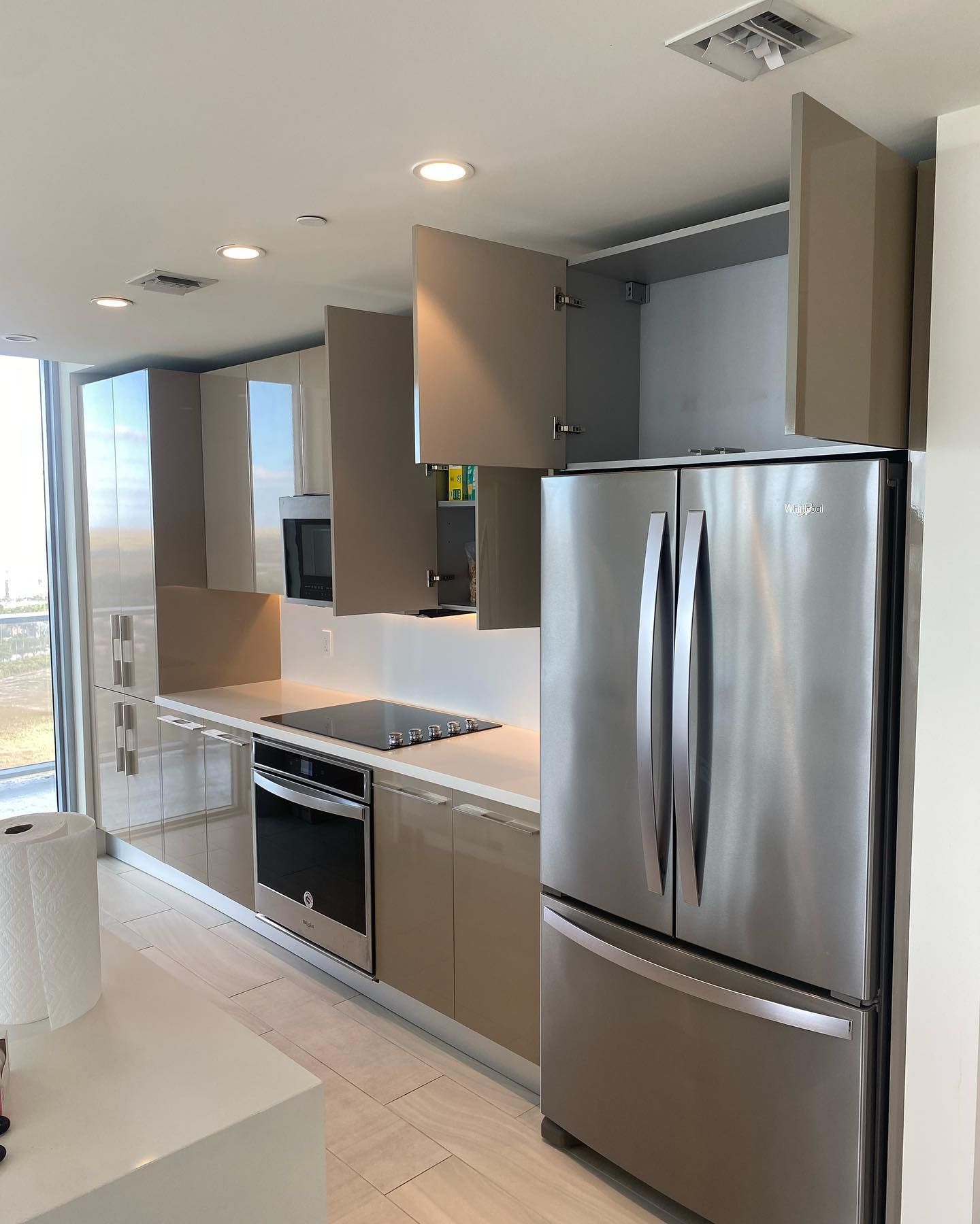 Modern kitchen with stainless steel refrigerator, tan cabinets, and white countertops.