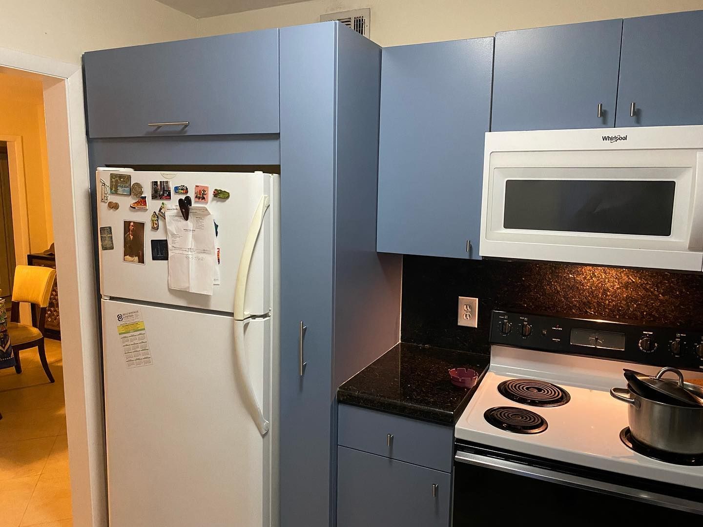 Kitchen with white refrigerator, blue cabinets, and a black countertop next to a white stove.