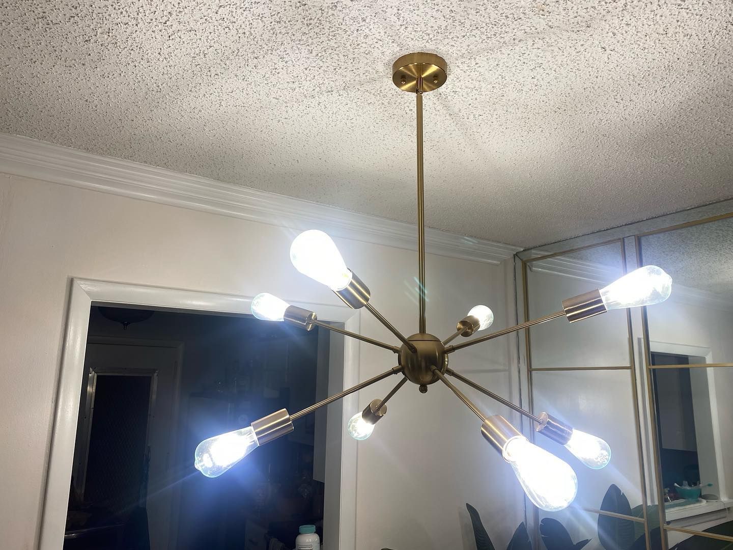 A gold, sputnik-style chandelier with eight exposed light bulbs hangs from a white ceiling.