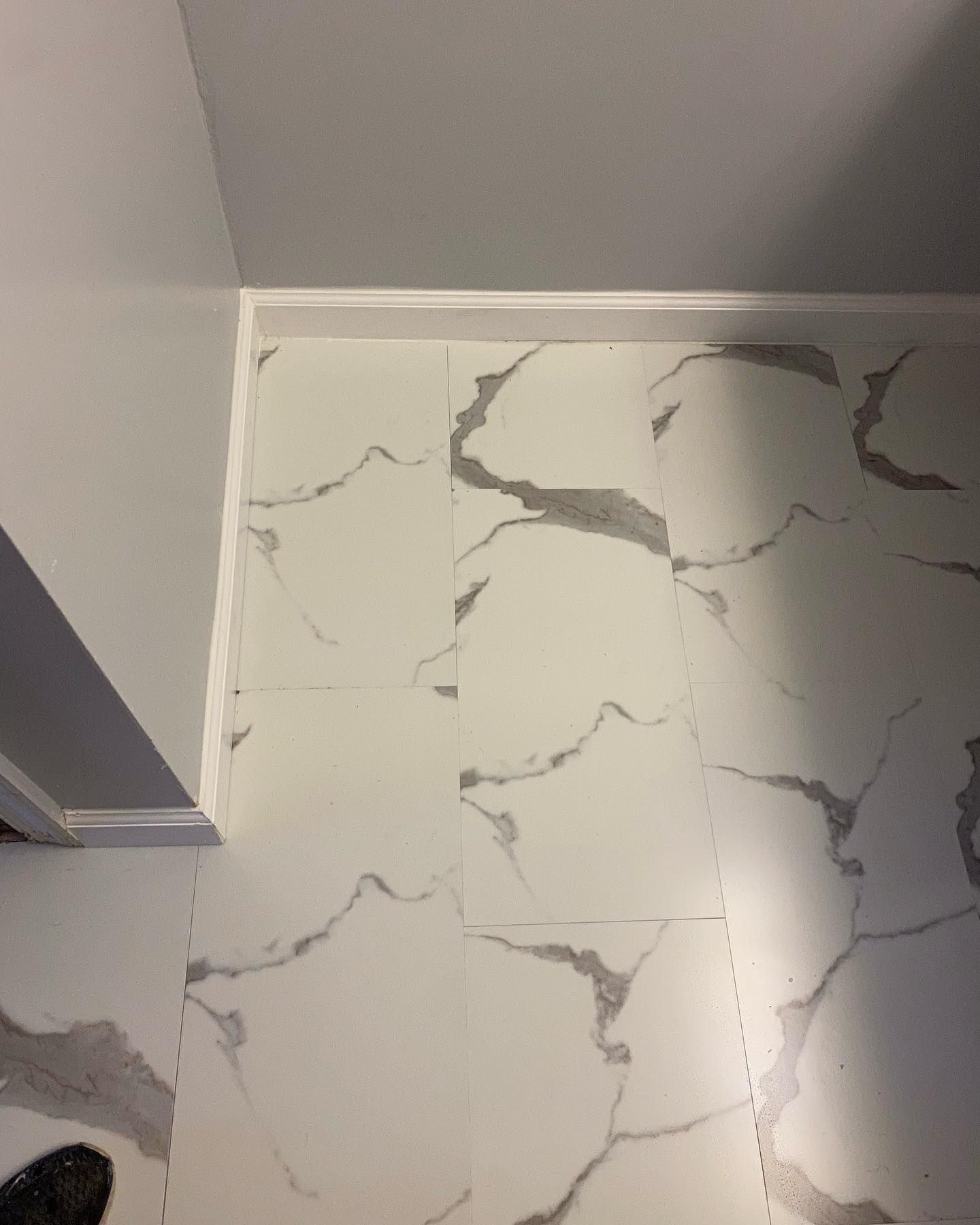 White marble-look floor tiles with gray veining, near a white wall and molding.