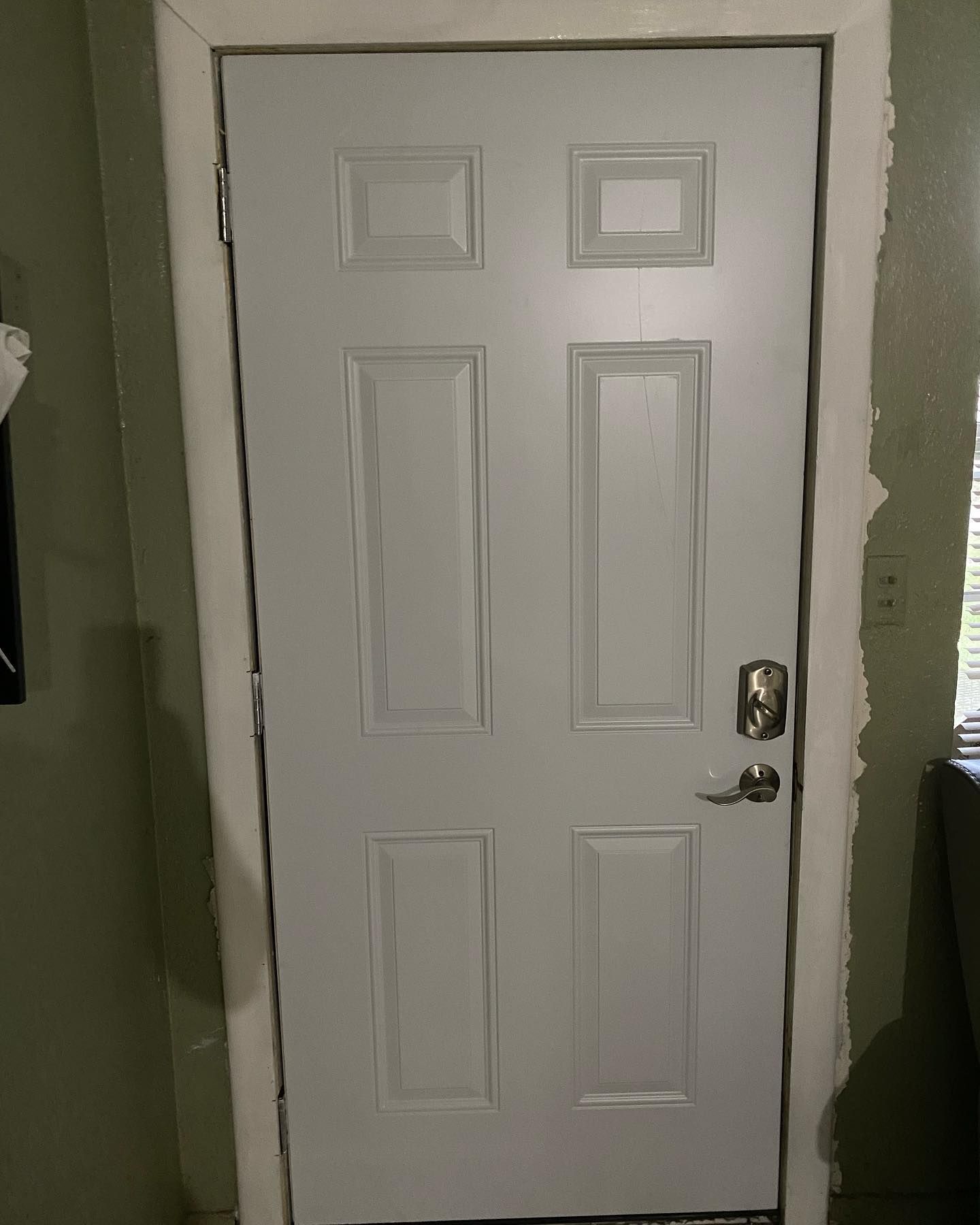 White six-panel door with digital lock and handle, set in a white frame against green walls.