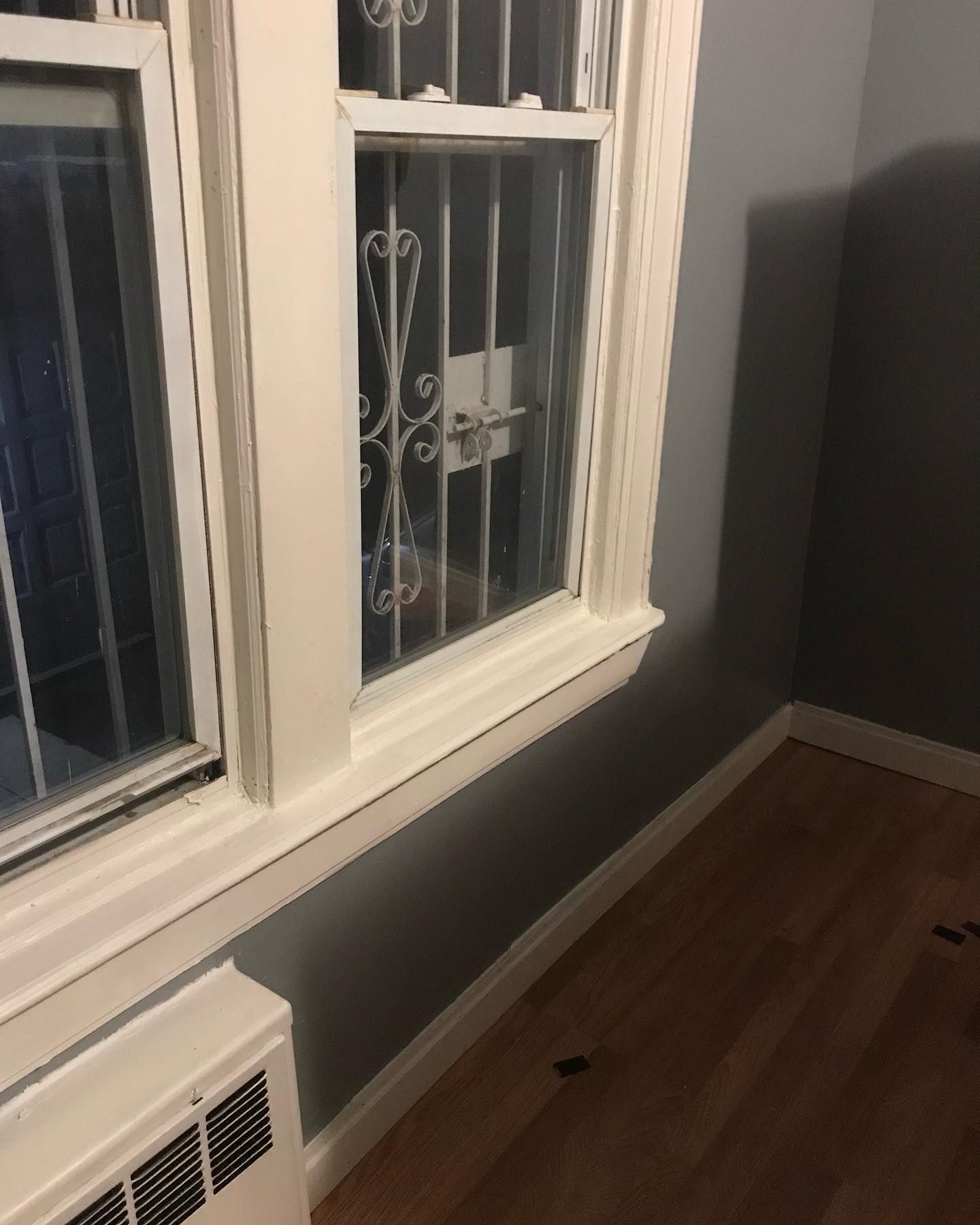 Window with security bars, gray walls, white trim, and a heater below the window.