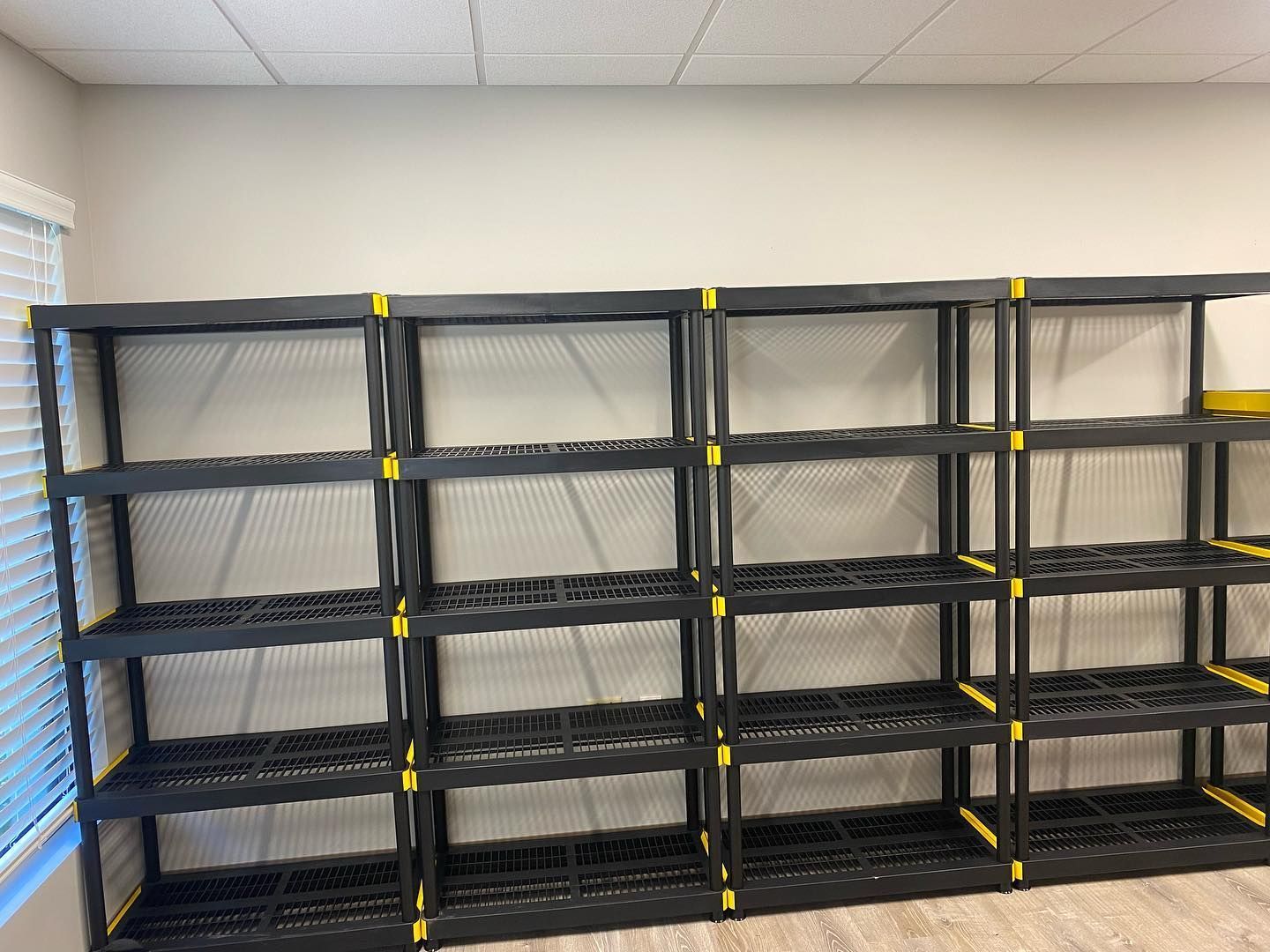 Black plastic shelving units against a light-colored wall, near a window with blinds.