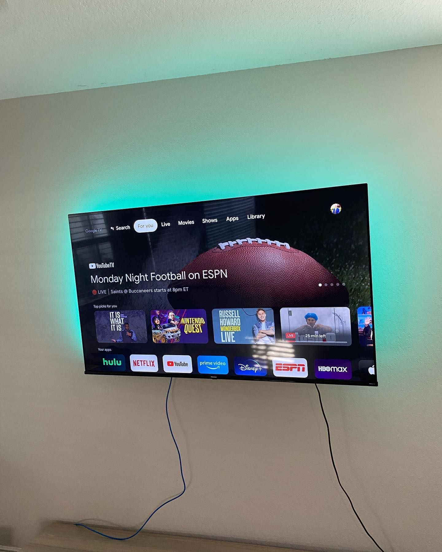 A flat-screen TV on a wall with green LED backlighting, displaying a football game.