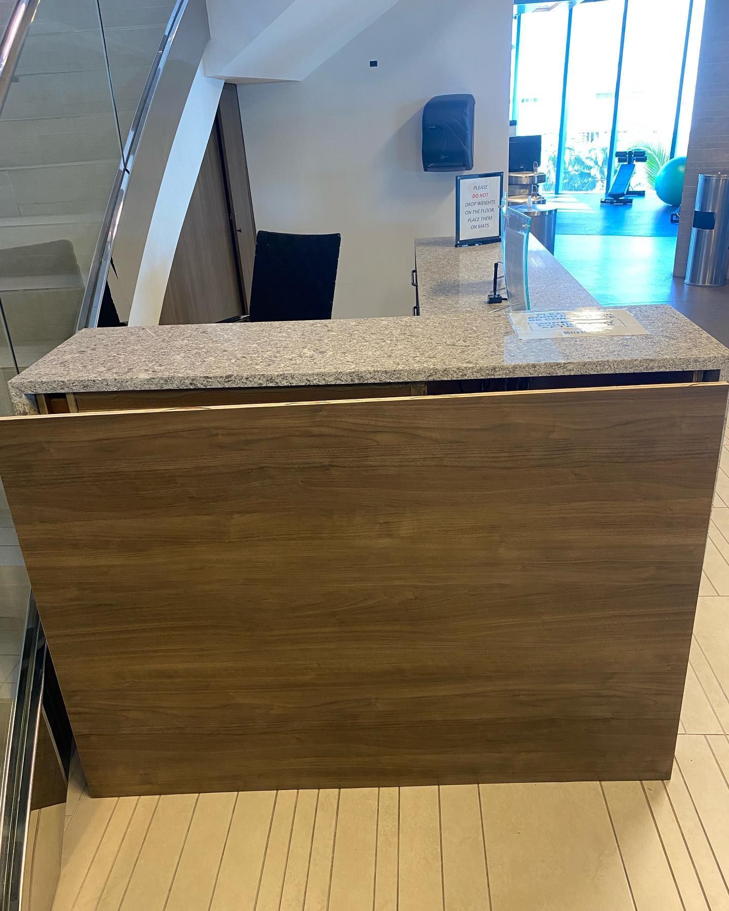 Reception desk with granite countertop and wood paneling. Stairs, door and outdoor view in background.
