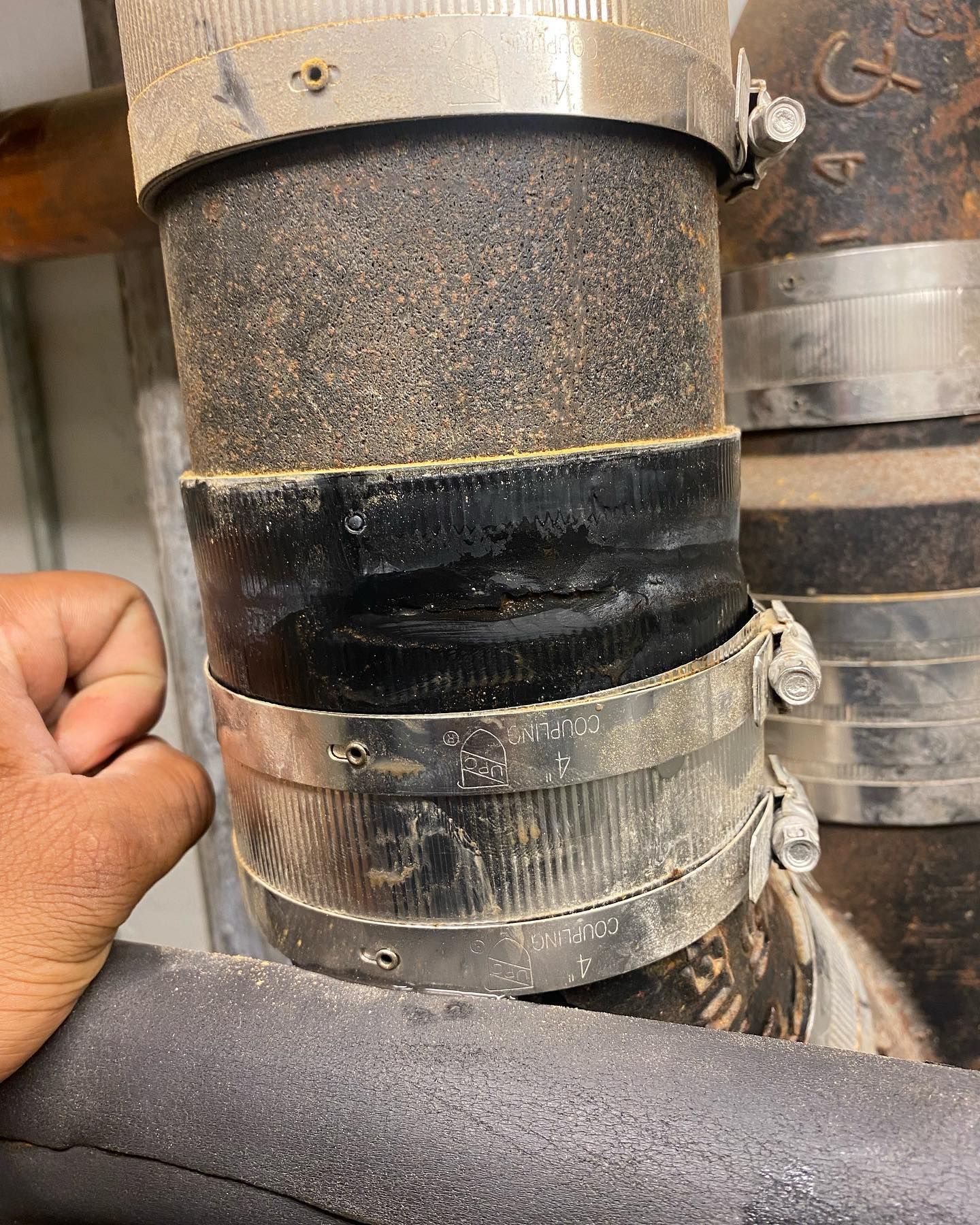 Close-up of black rubber coupling connecting two pipes, held together with metal clamps, hand visible.