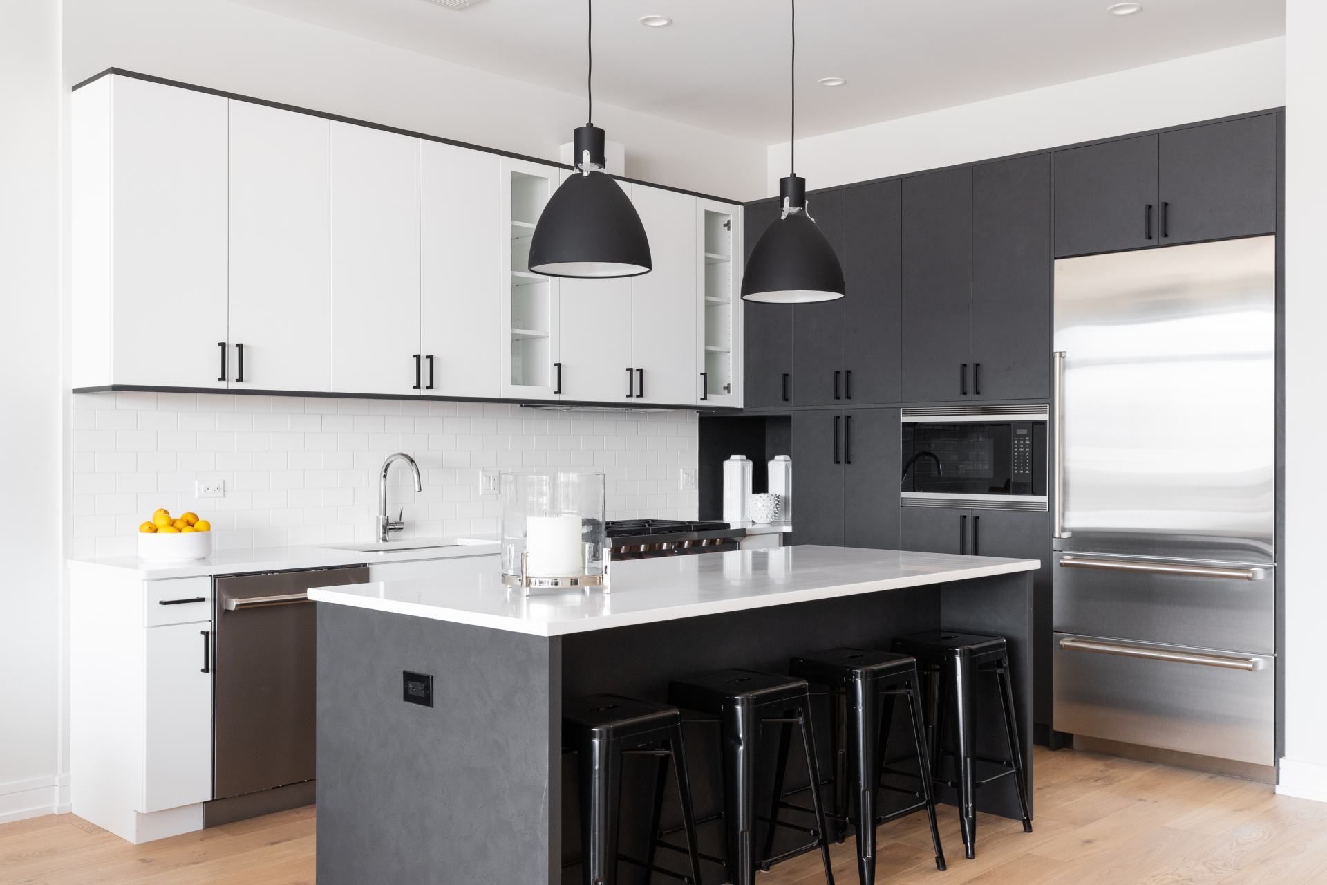 Modern kitchen with white and gray cabinets, island with black stools, stainless steel appliances.