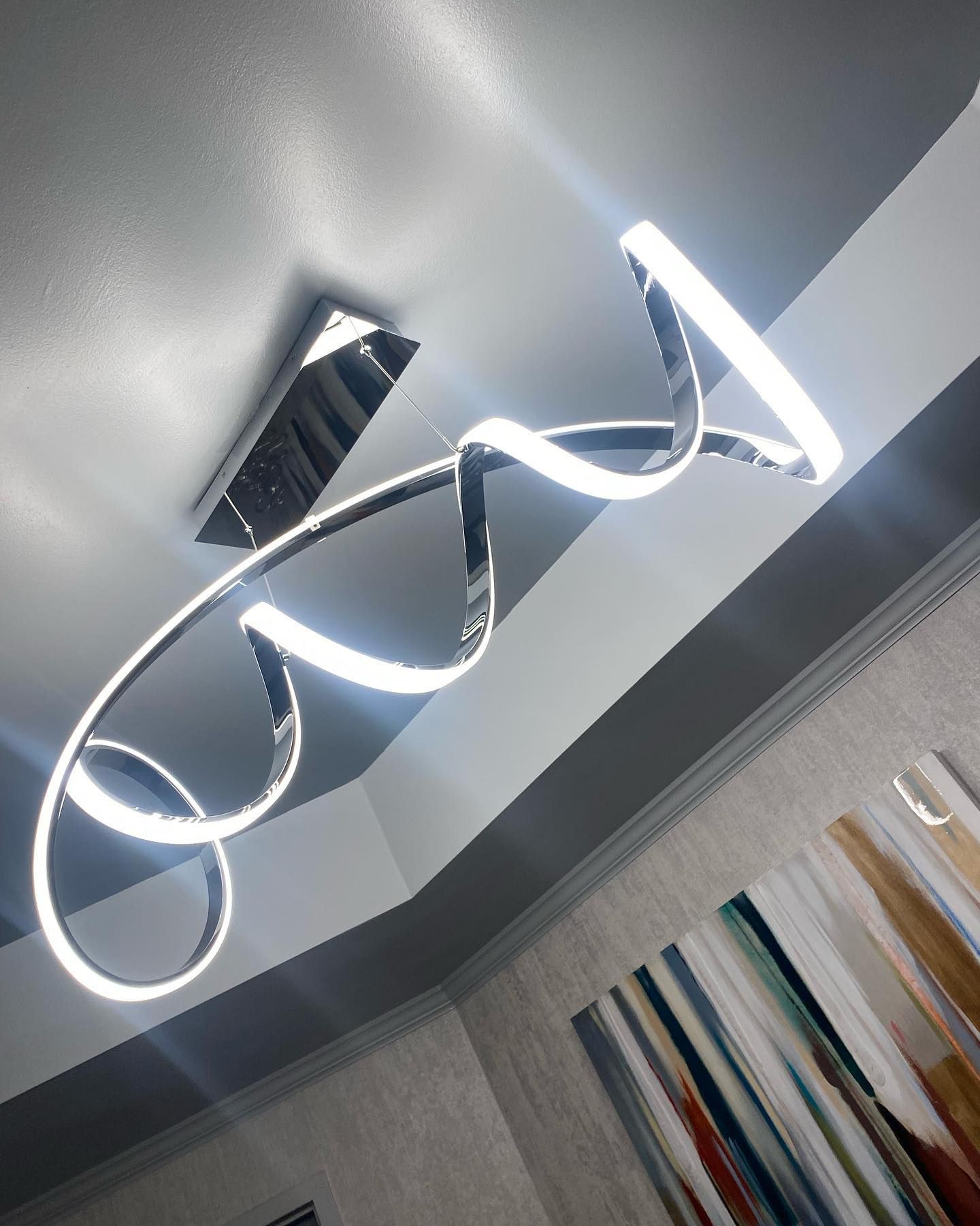 Chrome ceiling light with swirling, illuminated design in a modern living room.
