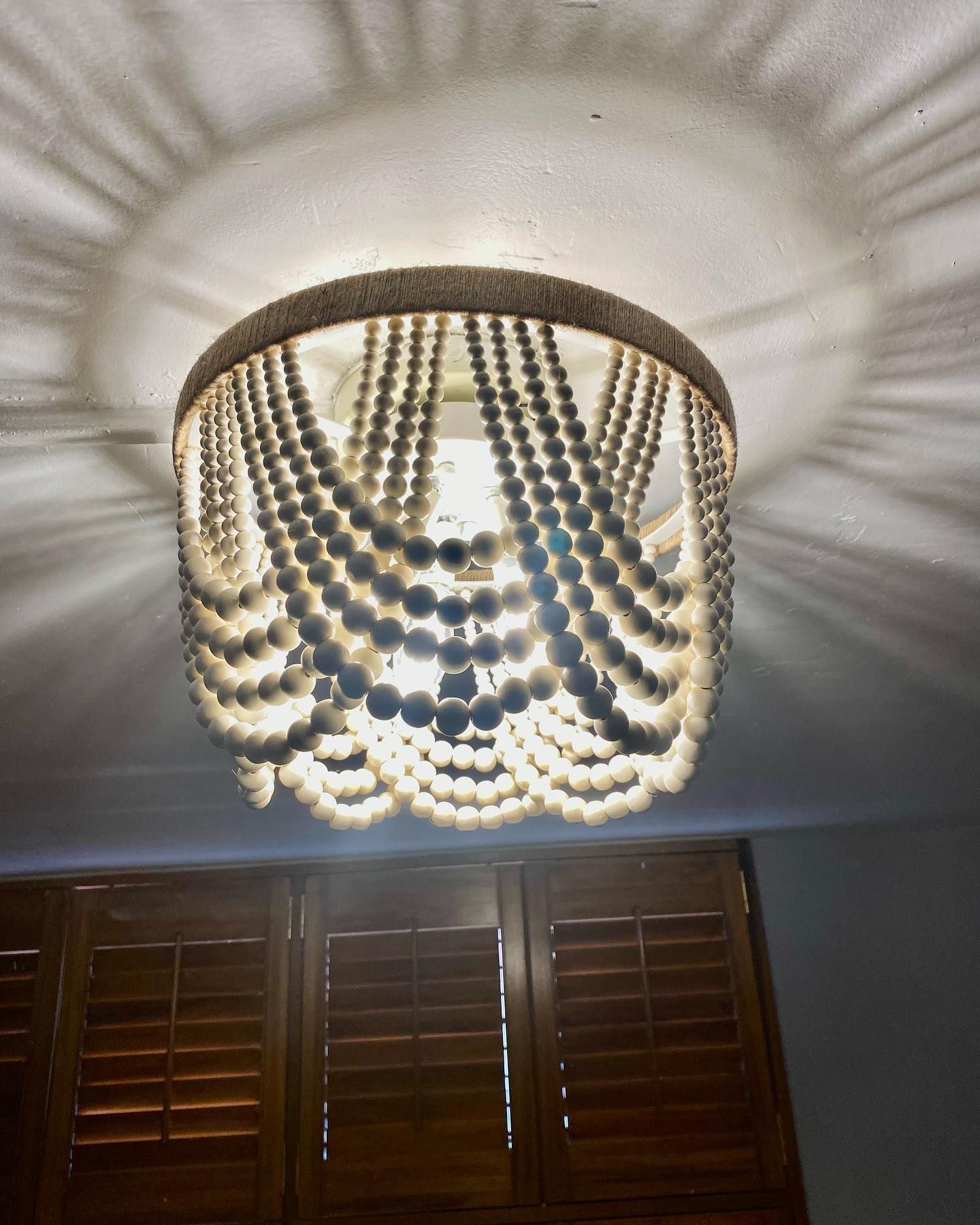Beaded pendant light fixture casting shadows, hanging above wooden blinds.