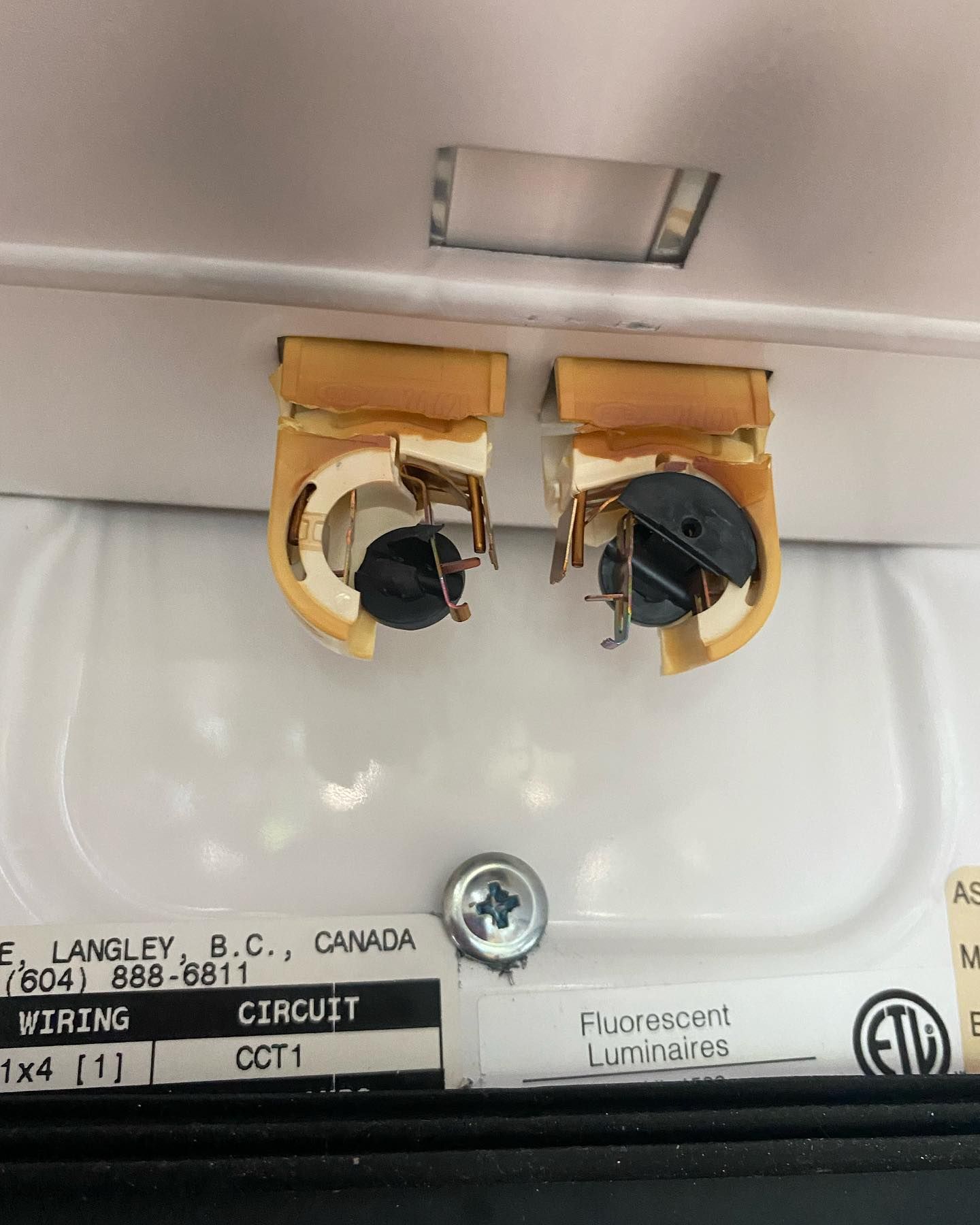 Close-up of a fluorescent light fixture showing two broken bulb holders. Text label visible.