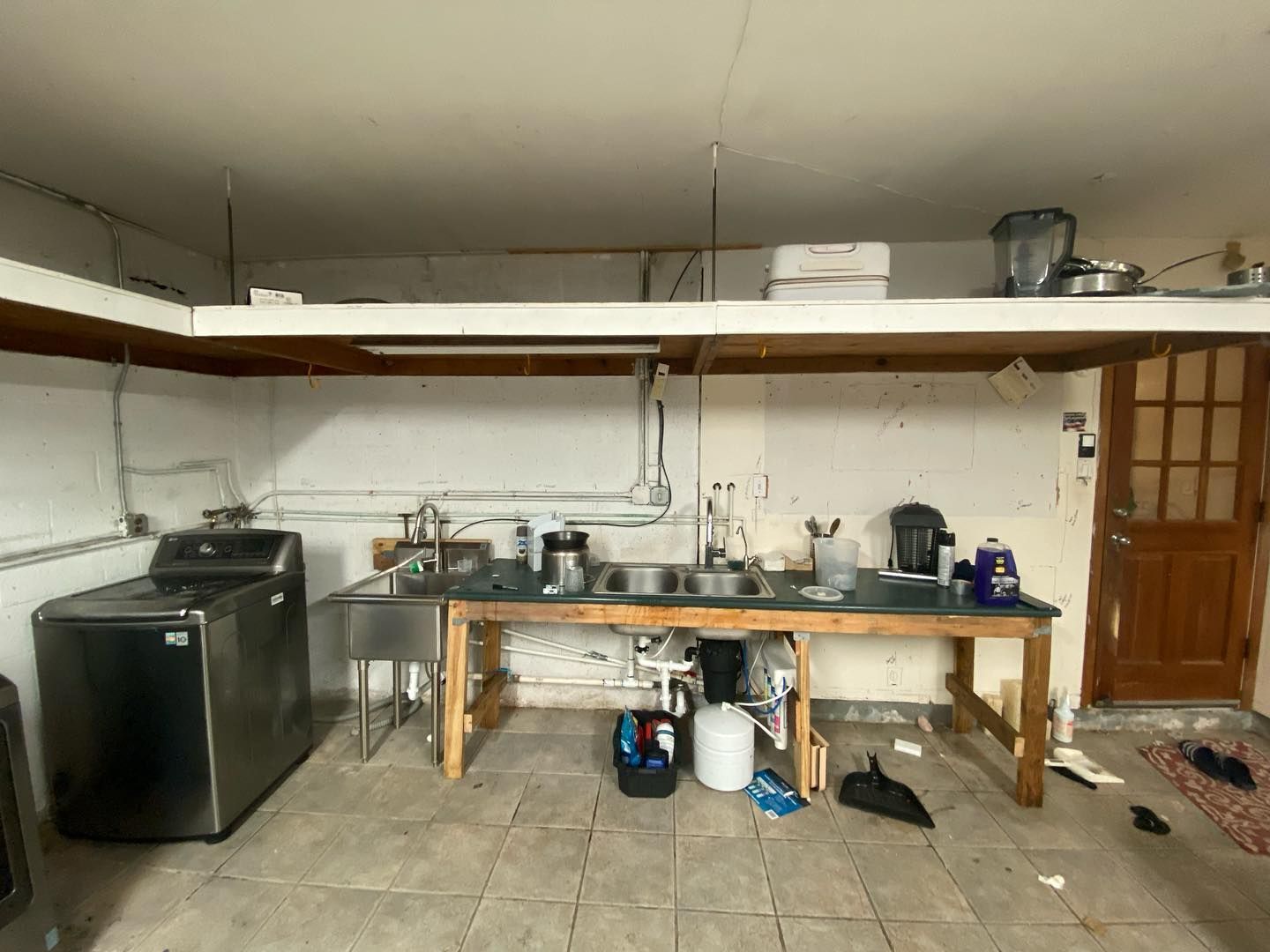 Laundry and kitchen setup in a basement. Washer, sink, and countertop are visible. Door to the right.