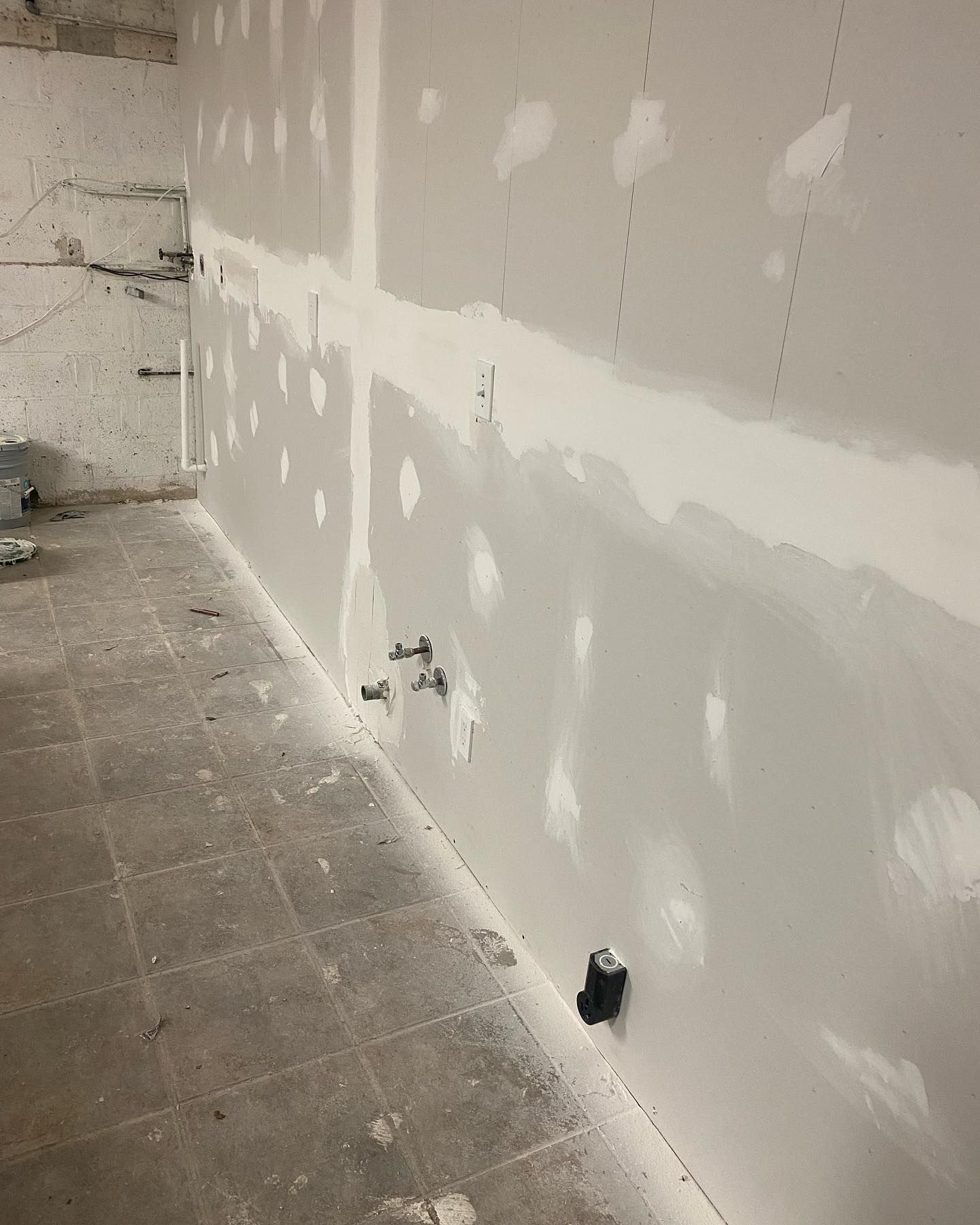 Drywall installed in a room under construction; various electrical and plumbing fixtures are visible.