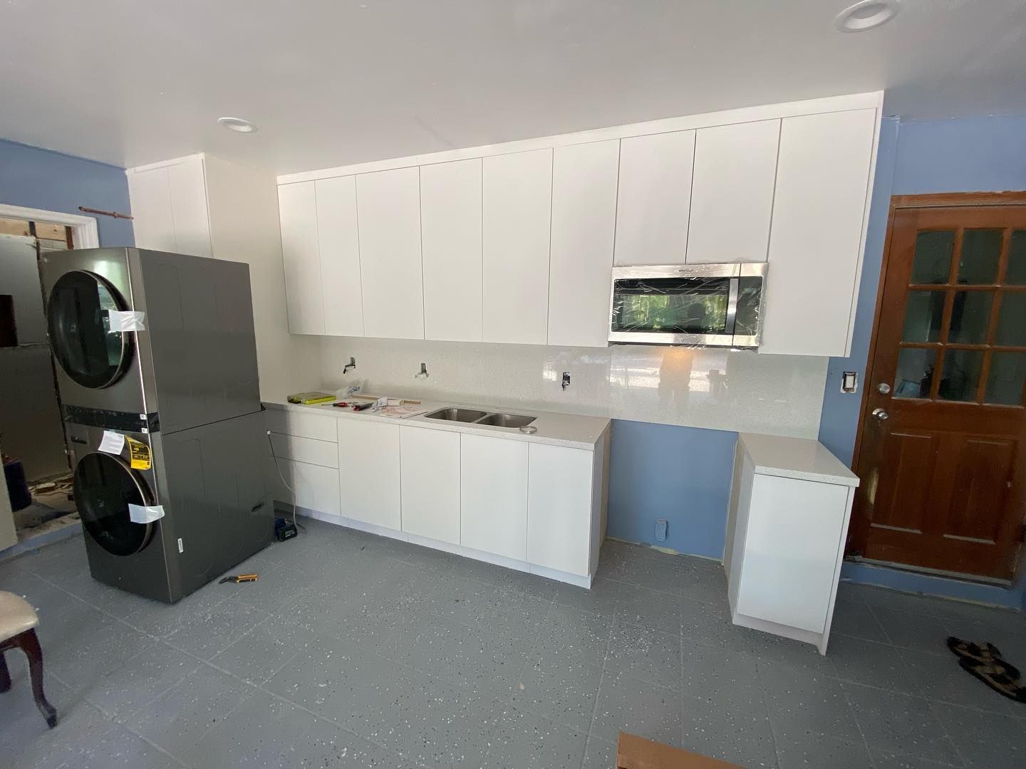 White kitchen cabinets with a microwave, washer/dryer unit, and gray floor in a renovated space.