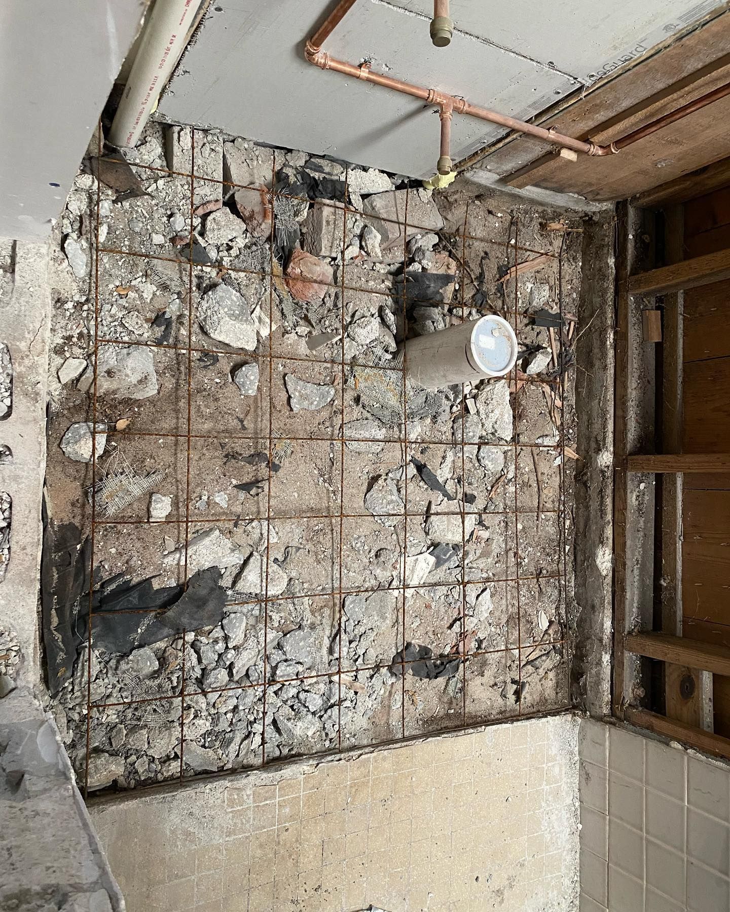 Exposed bathroom wall with stones, metal grid, copper pipes, and a white pipe.