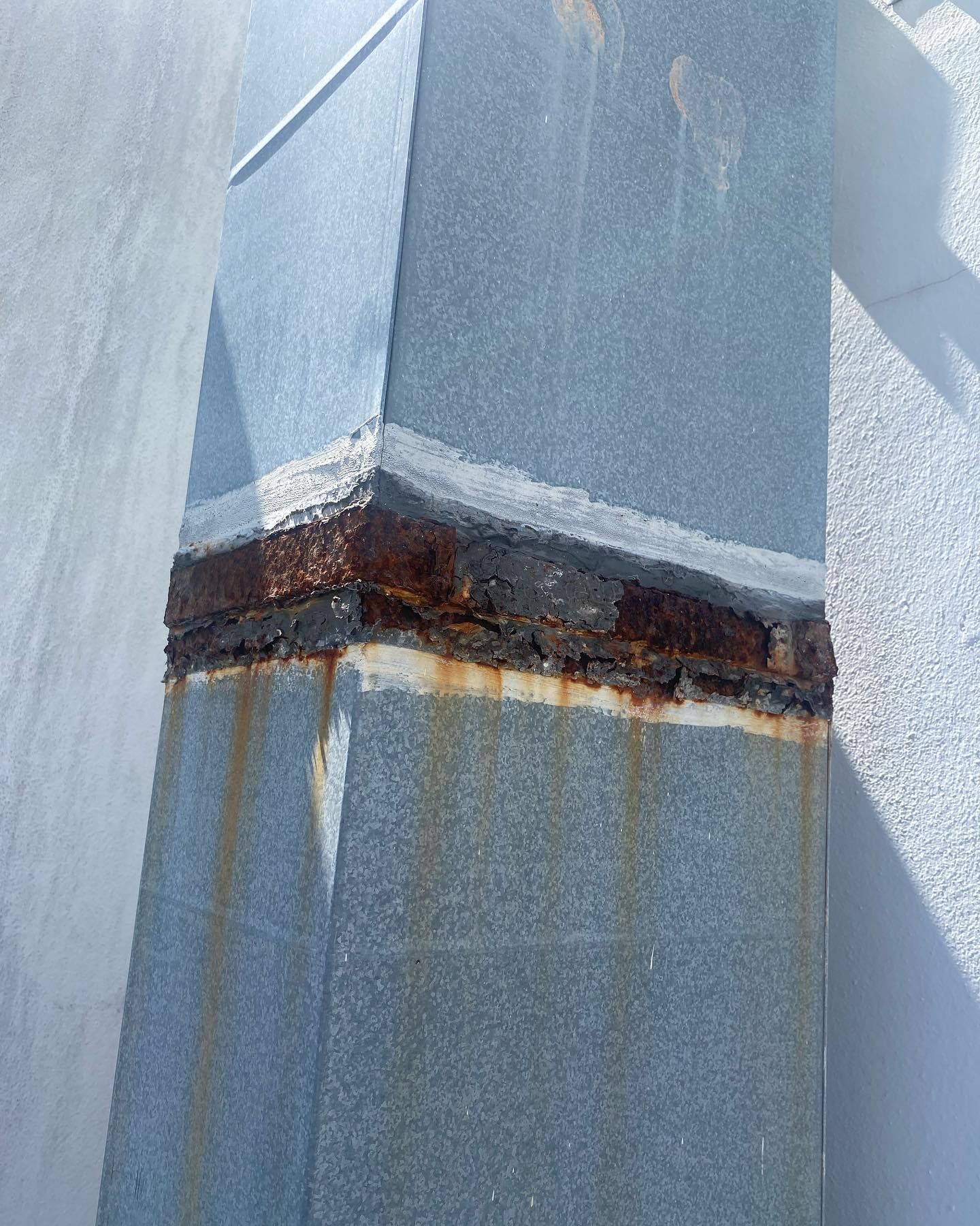 Rusted metal vent section with corrosion and water stains against a white wall.