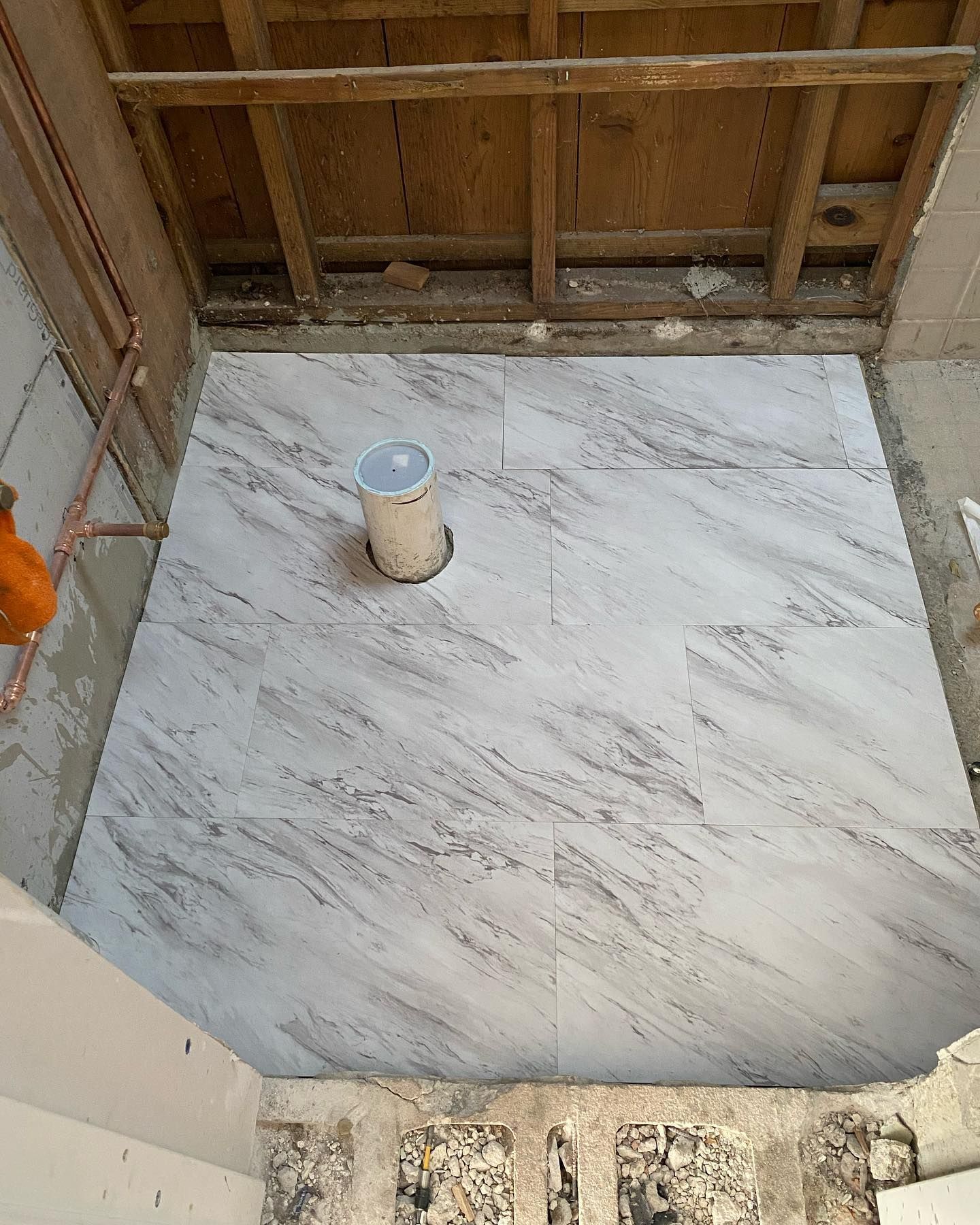 Newly tiled bathroom floor, with pipe and unfinished ceiling visible.