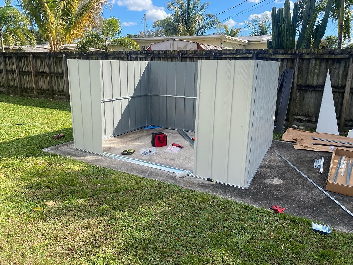 Partially assembled shed on a concrete pad in a grassy backyard, tools visible.