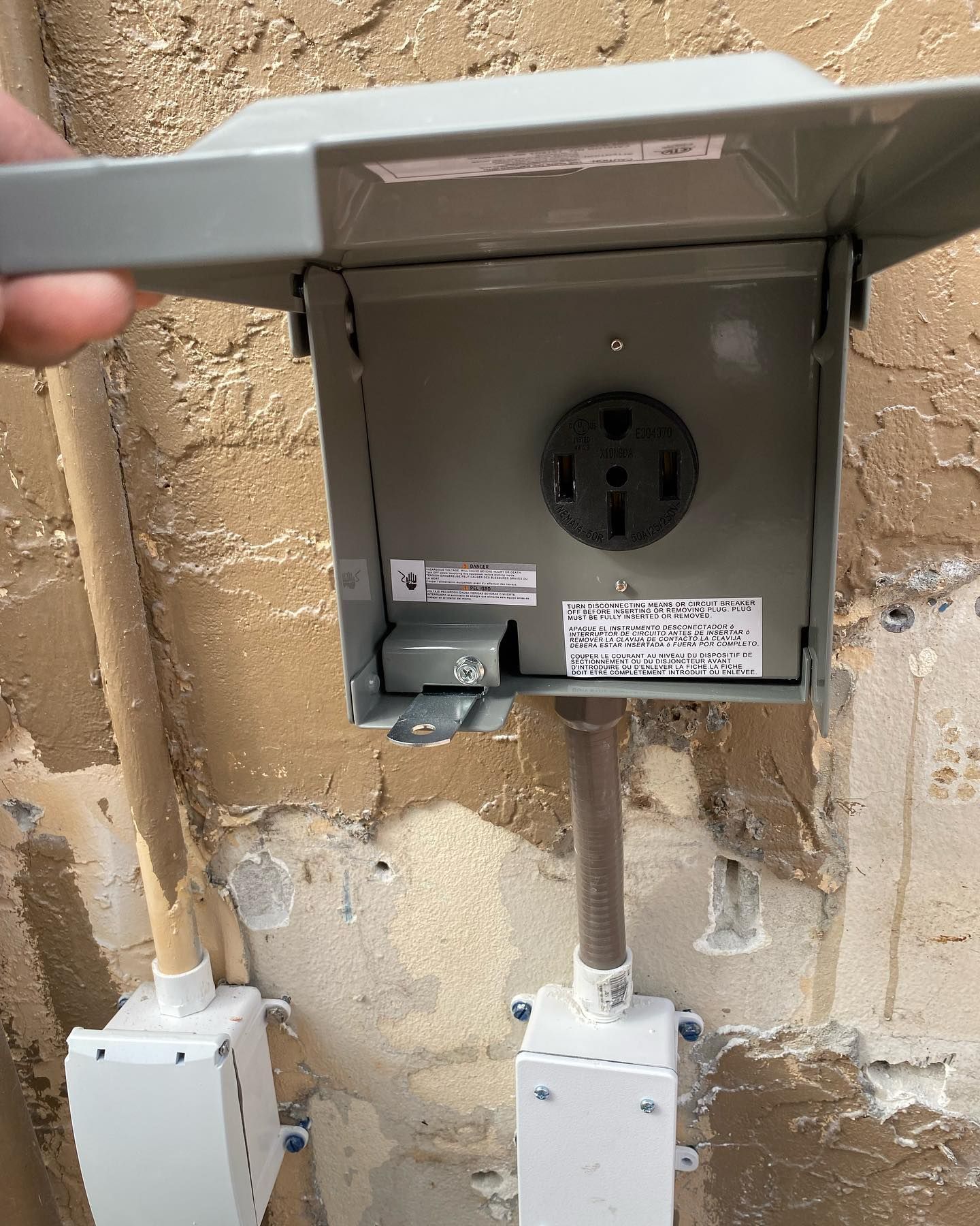 Gray electrical outlet box mounted on a textured wall, with a brown pipe and attached conduit boxes.