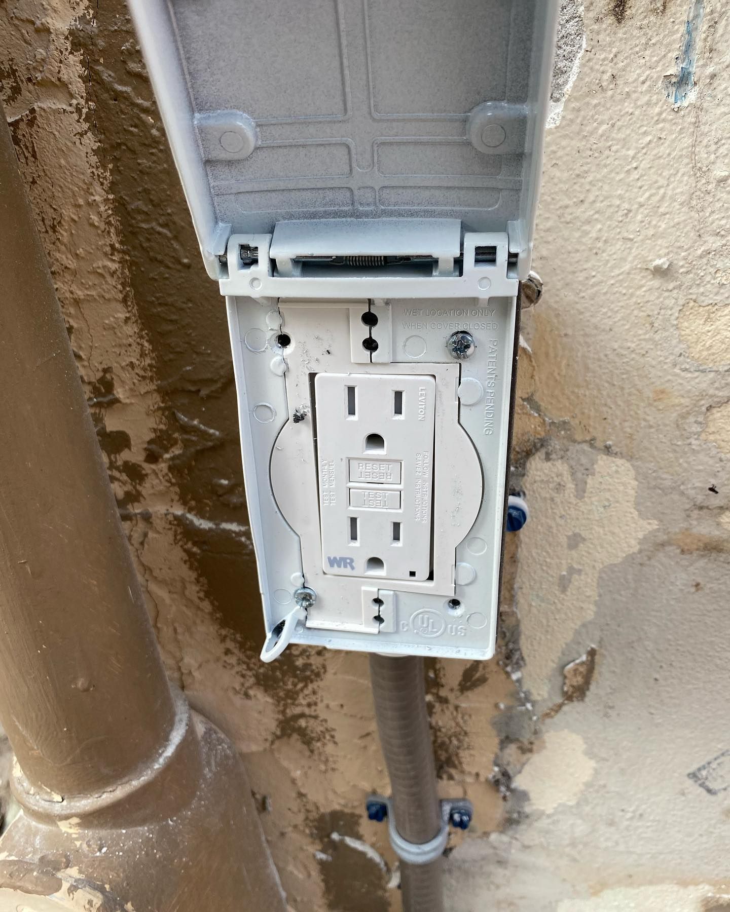 White weatherproof electrical outlet box mounted on a wall with the cover open.