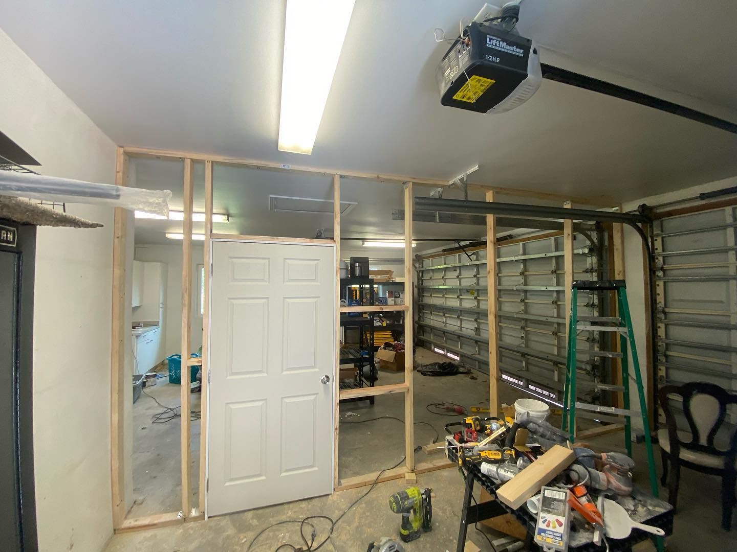 Garage interior with partial framing of walls, a white door, and tools scattered about.
