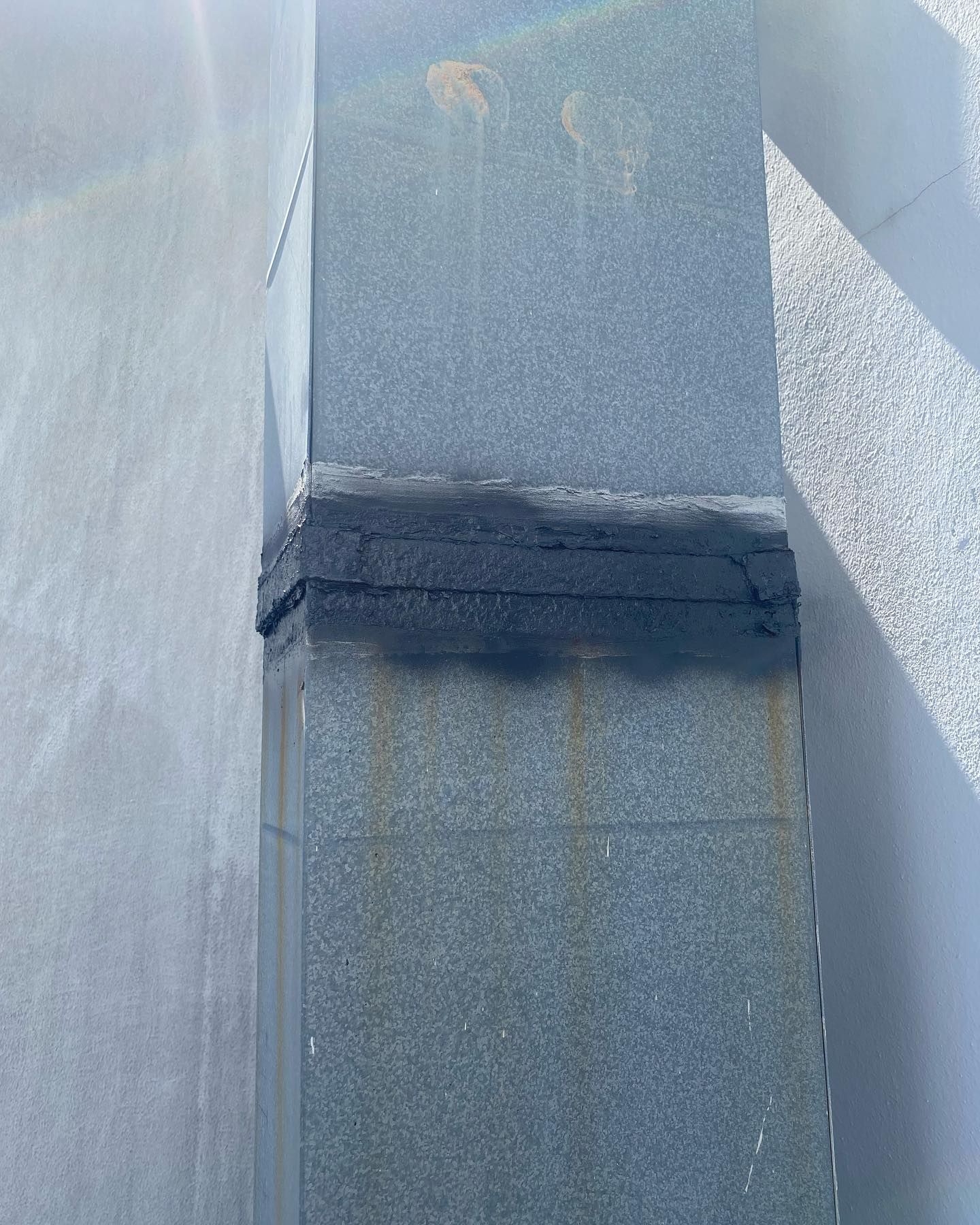 Gray metal ductwork, with a black sealant band, attached to a light-colored wall.