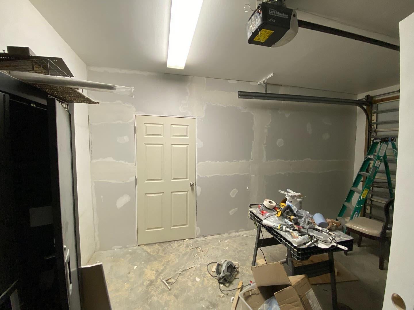 Garage interior with drywall on walls, tools on a table, and a door.