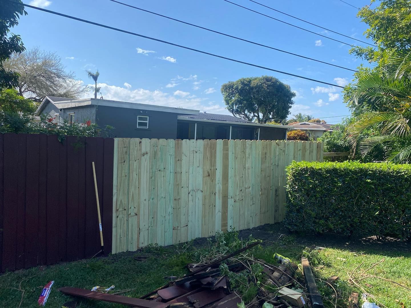 Wooden fence, partially painted brown, next to unpainted wood, with a house in the background.