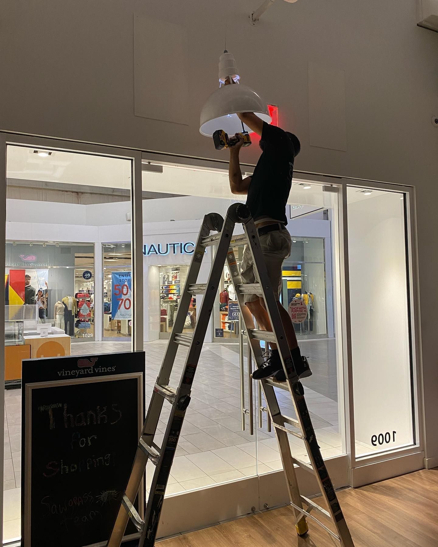 Person on a ladder installing a light fixture inside a retail store.